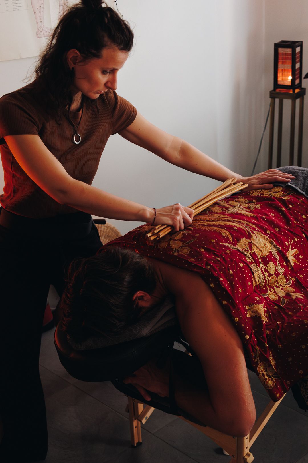 Massage therapist using bamboo sticks to perform a back massage on a seated client.