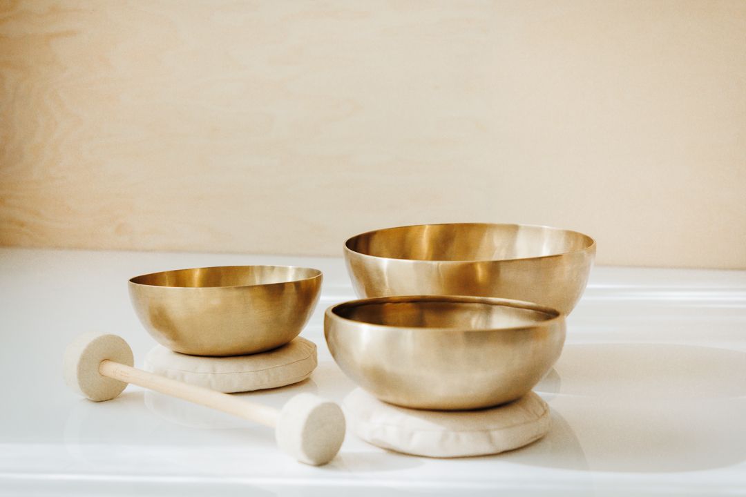 Three golden brass singing bowls of varying sizes displayed on white surface with wooden mallets for sound healing meditation.
