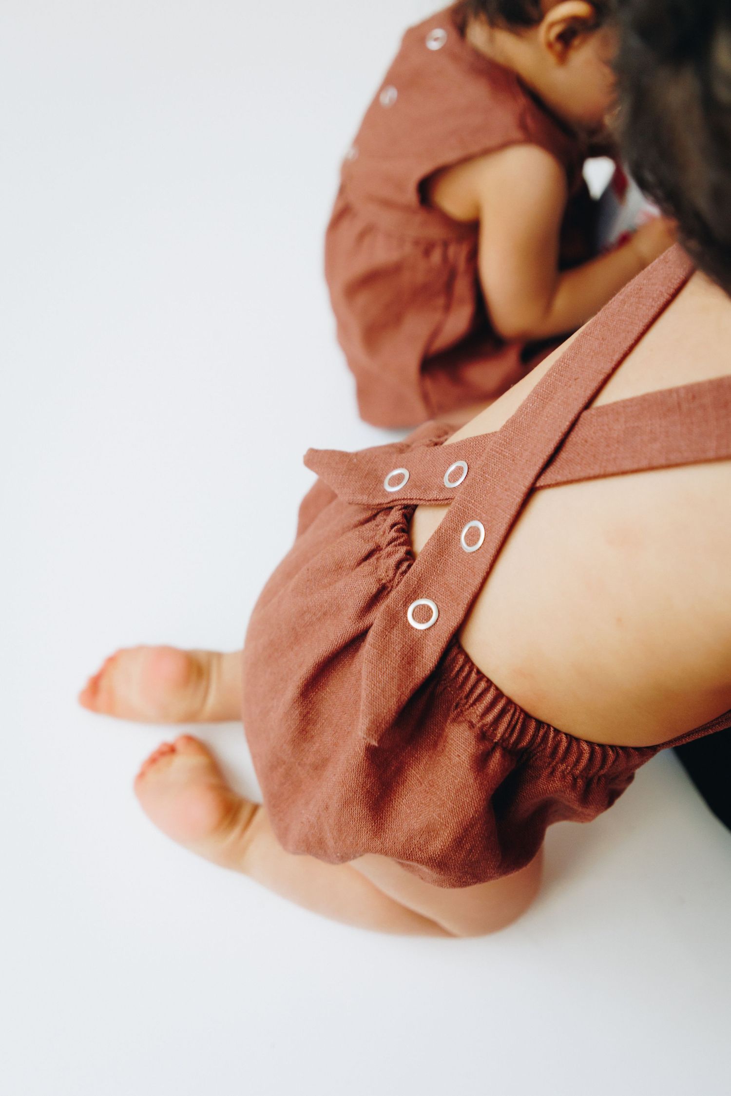 Baby wearing a rust brown linen romper with snap buttons, seated on a white background.