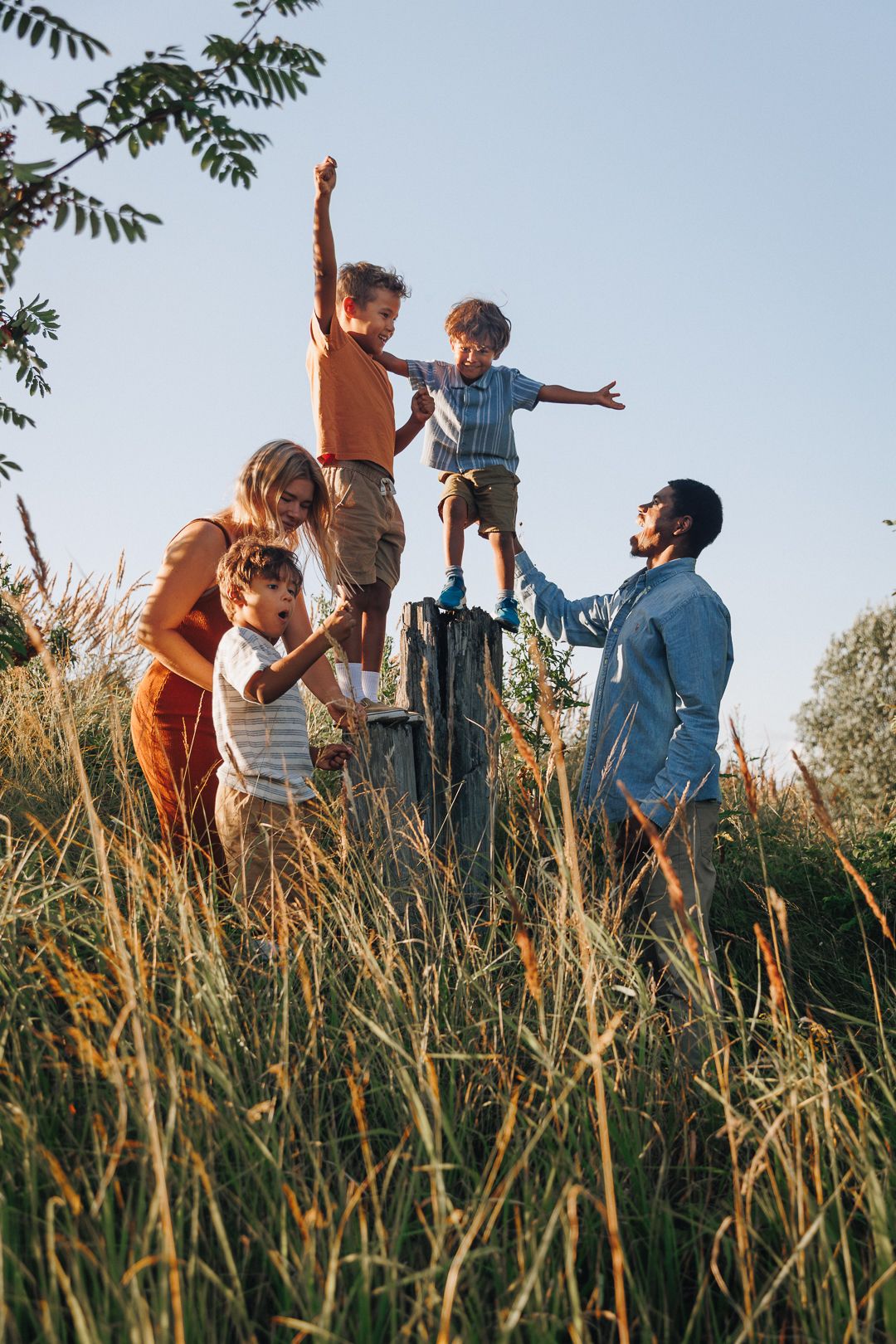 Family plays and leaps joyfully together in tall summer grass during golden hour in a candid lifestyle series.