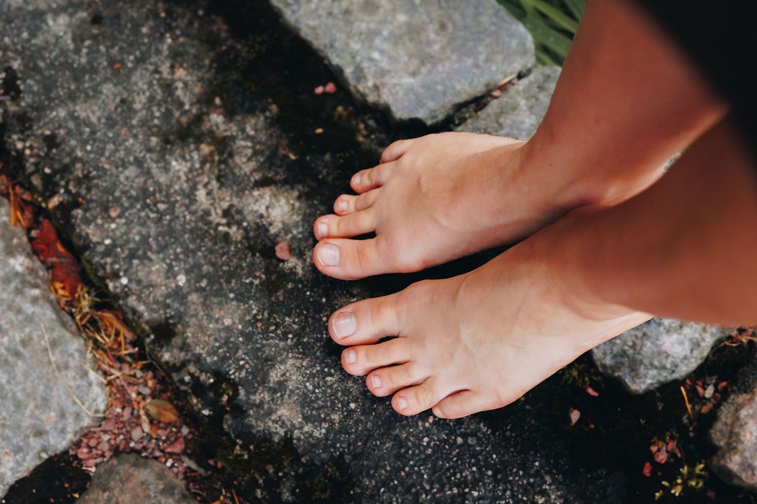 Bare feet standing on wet stone ground outdoors, with natural toenails and tanned skin visible from above.