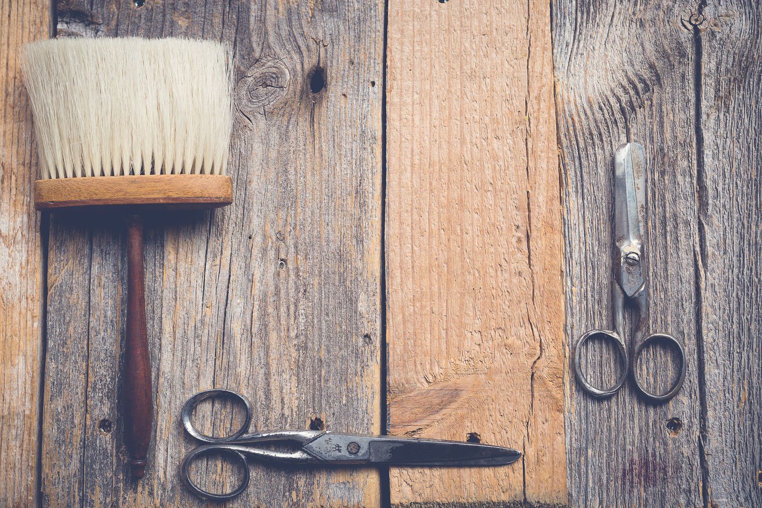Vintage barber tools including two scissors and a brush arranged on a rustic wooden background.