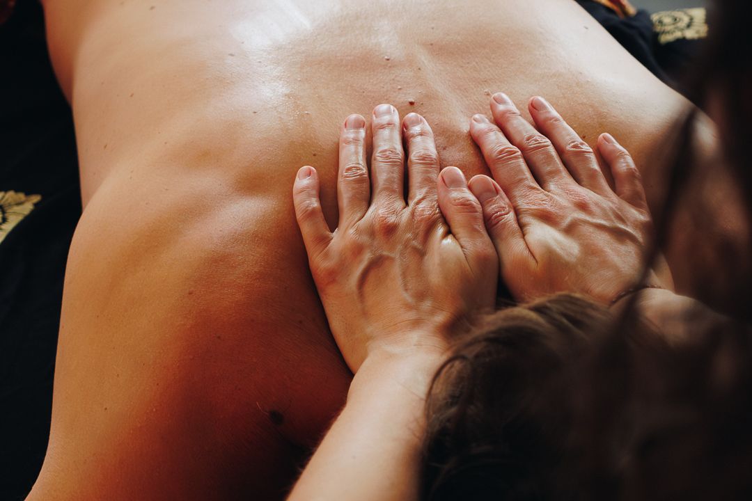 Close-up of therapist using both hands to massage client's upper back during spa treatment.