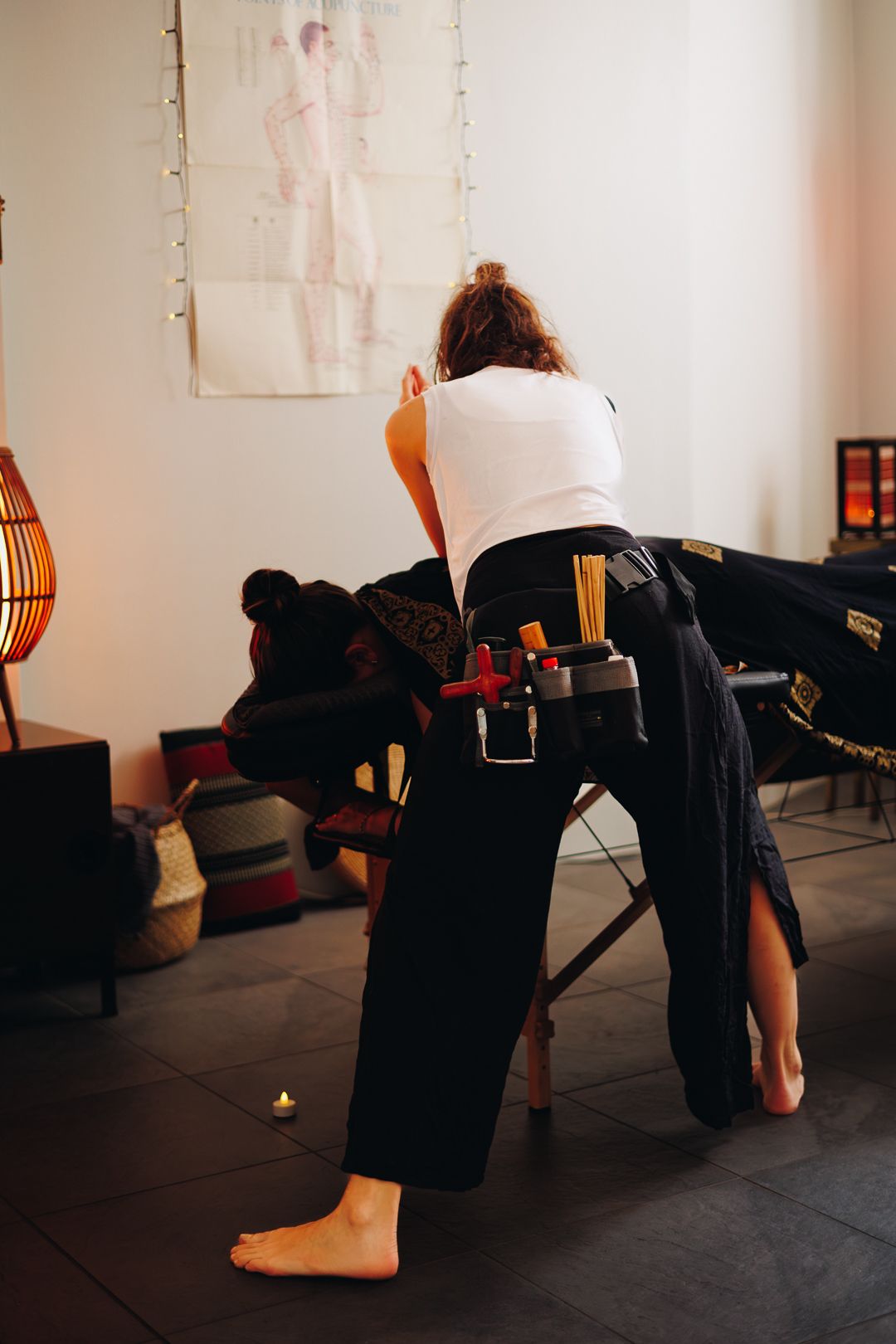 Barefoot massage therapist working on seated client using traditional Thai massage chair technique.