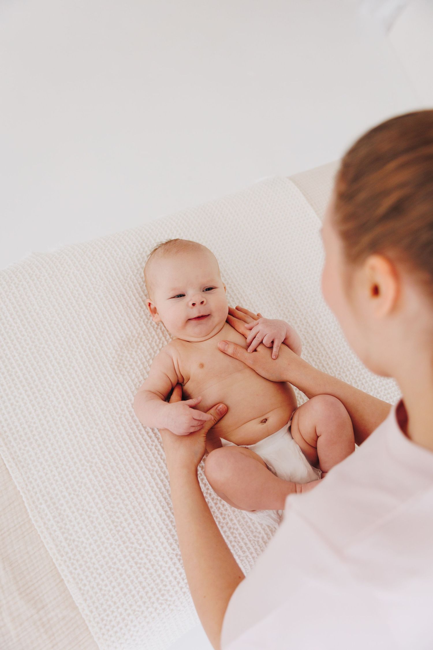 A healthcare professional performs a gentle infant massage on a newborn baby lying on a white textured blanket.