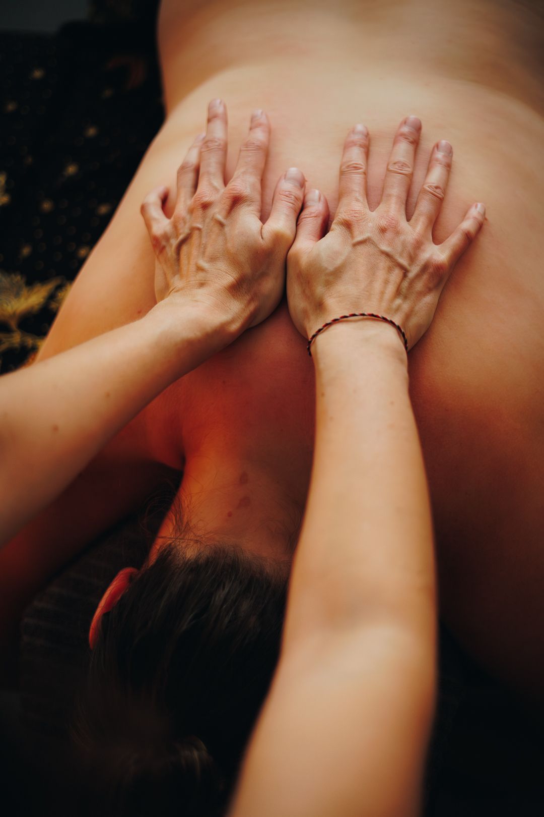 Close-up of a massage therapist using both hands to perform a deep tissue back massage on a client.