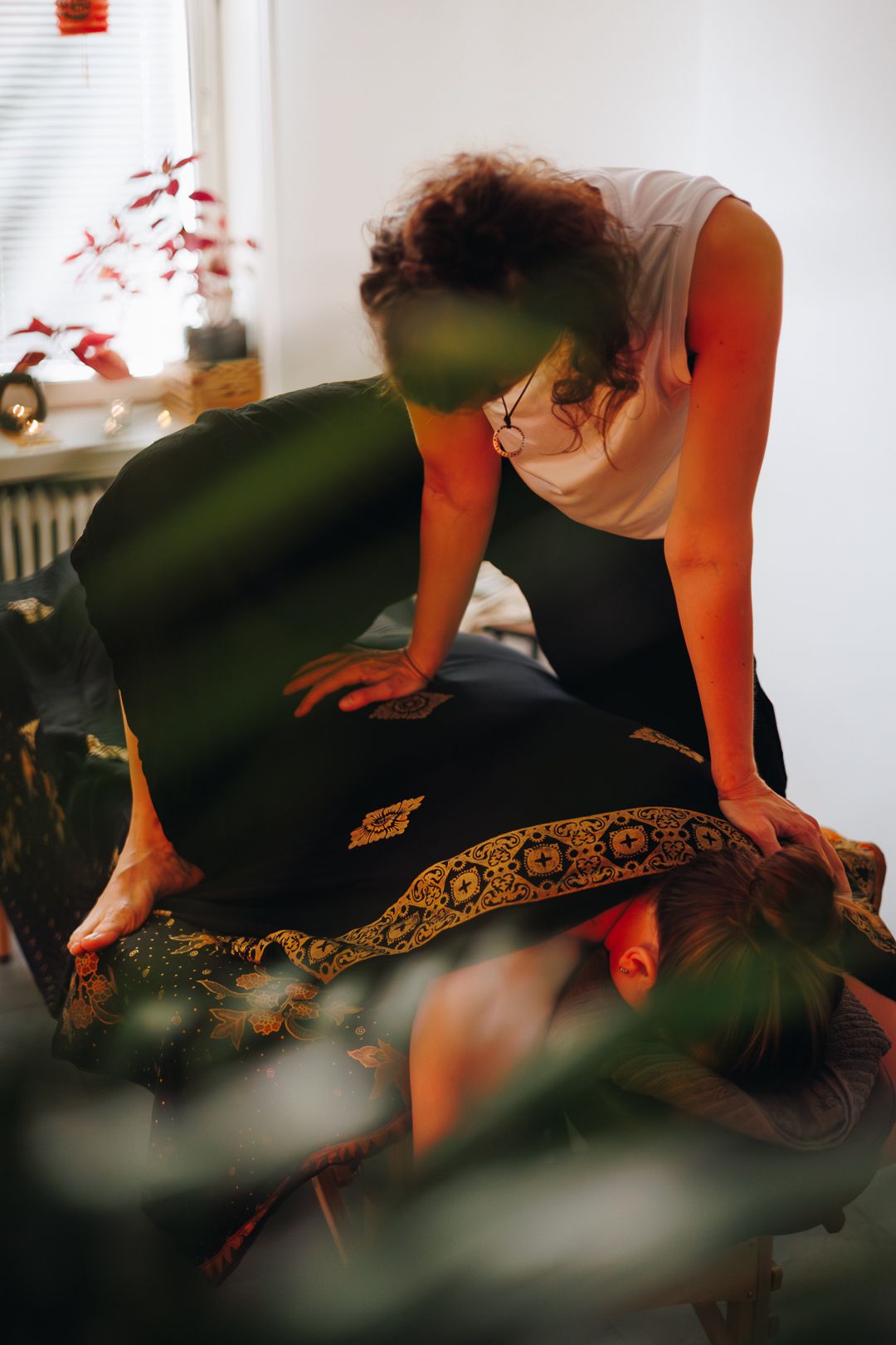Curly-haired therapist performing Thai massage on client lying on decorated mat on floor.