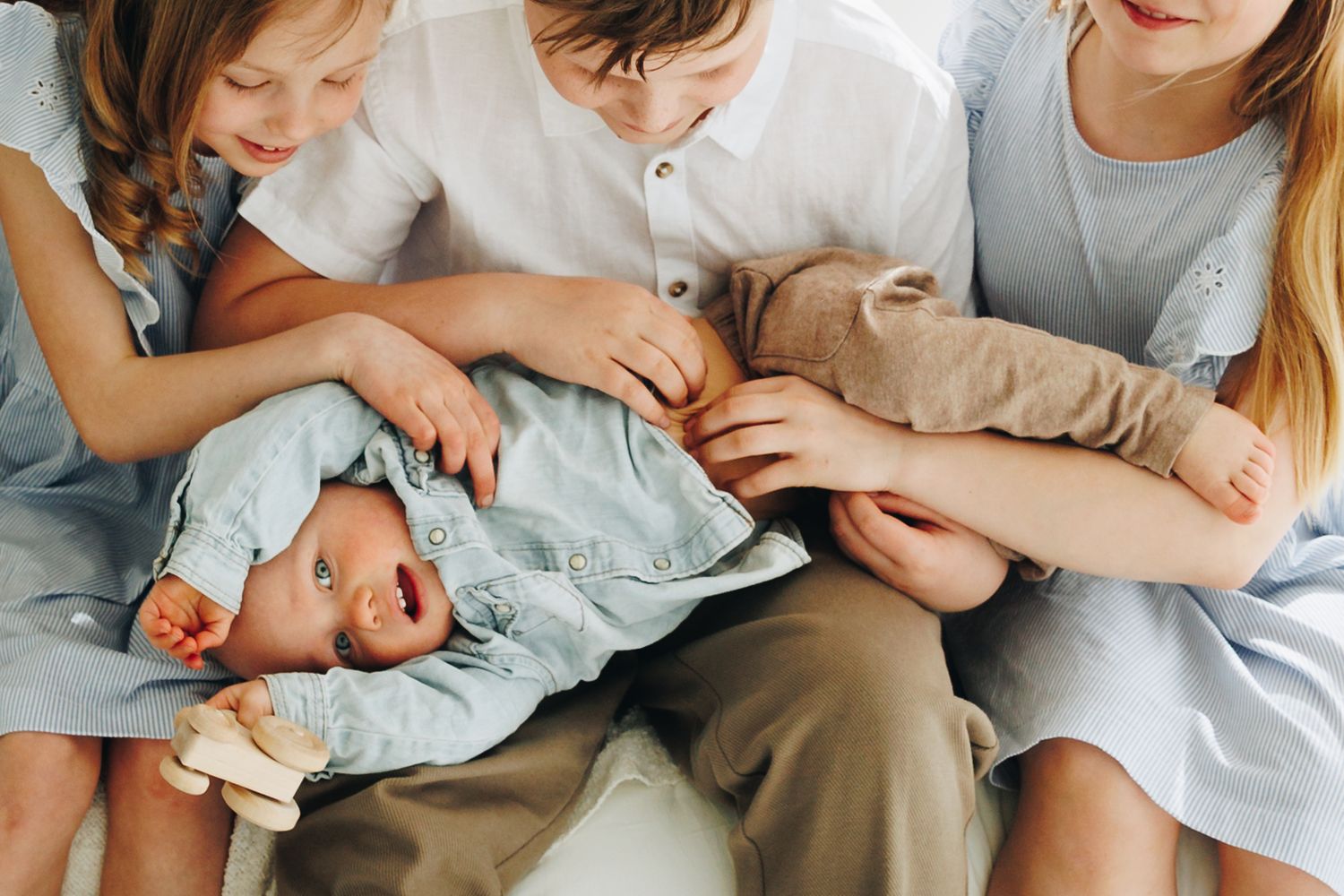 Three older siblings lovingly cradling a newborn baby dressed in blue, sharing a tender family moment together.