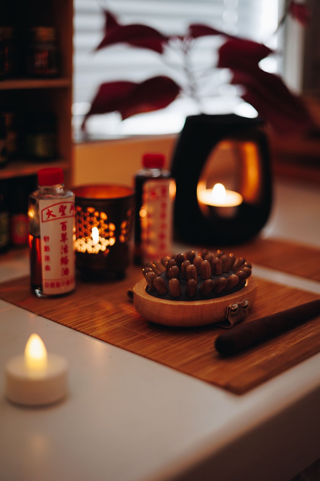 Cozy spa table with moxa sticks, candles, and Asian herbal bottles on bamboo mat in warm candlelight.