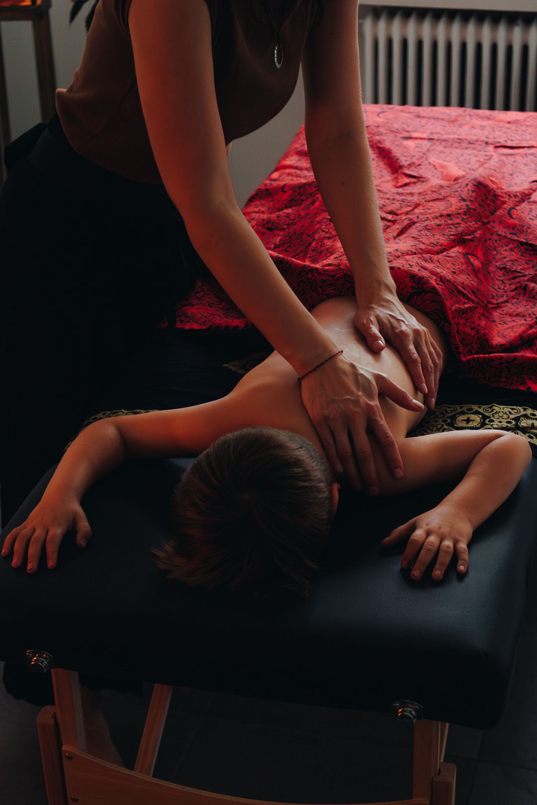 Professional massage therapist applying deep tissue back massage to a client on a dark massage table.