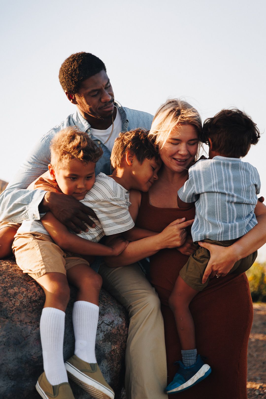 A group of friends huddle together in a candid embrace during sunset, showing warm companionship and joy.
