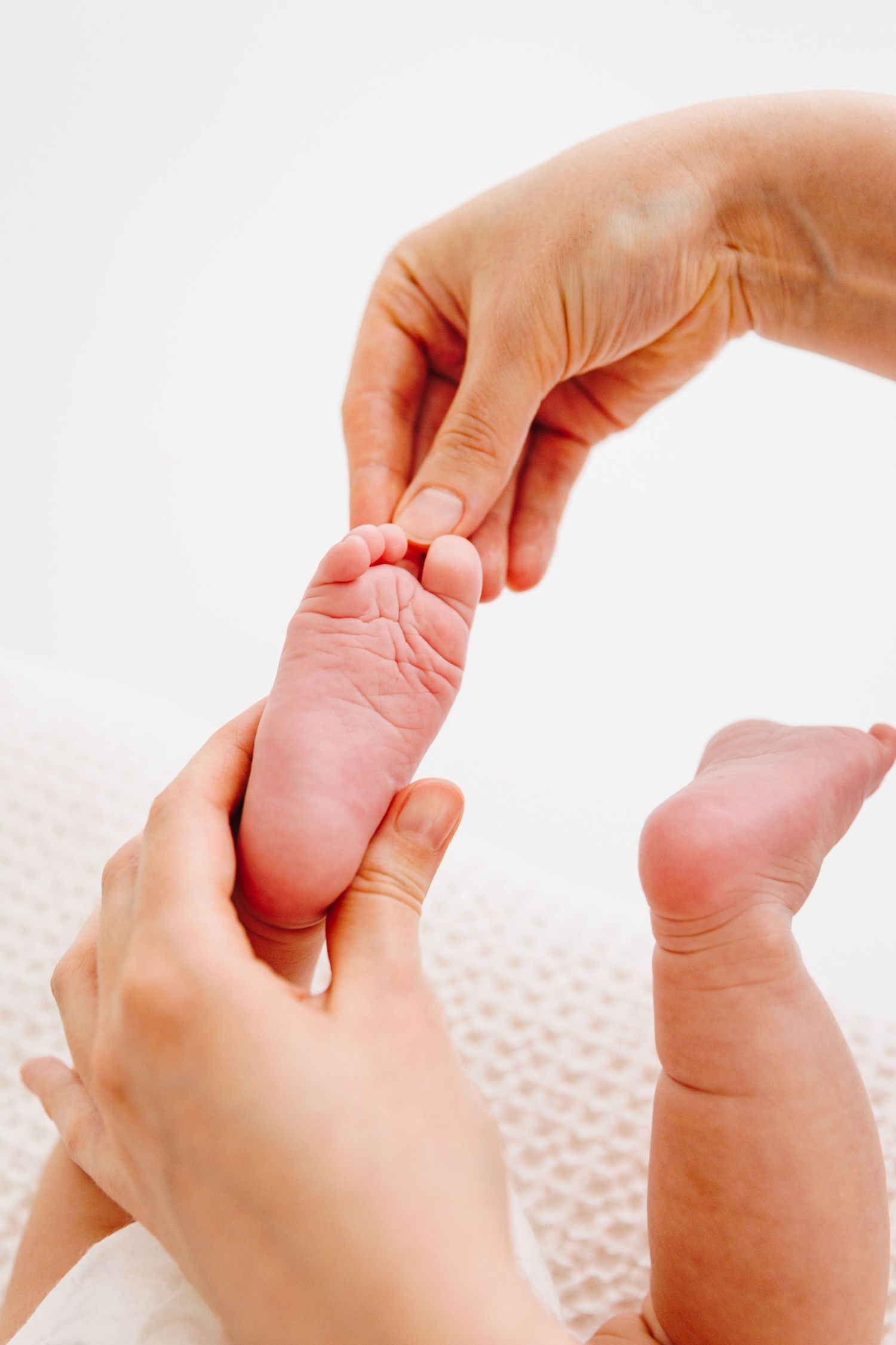 Adult hands gently massaging a newborn baby's tiny feet on a soft white blanket.
