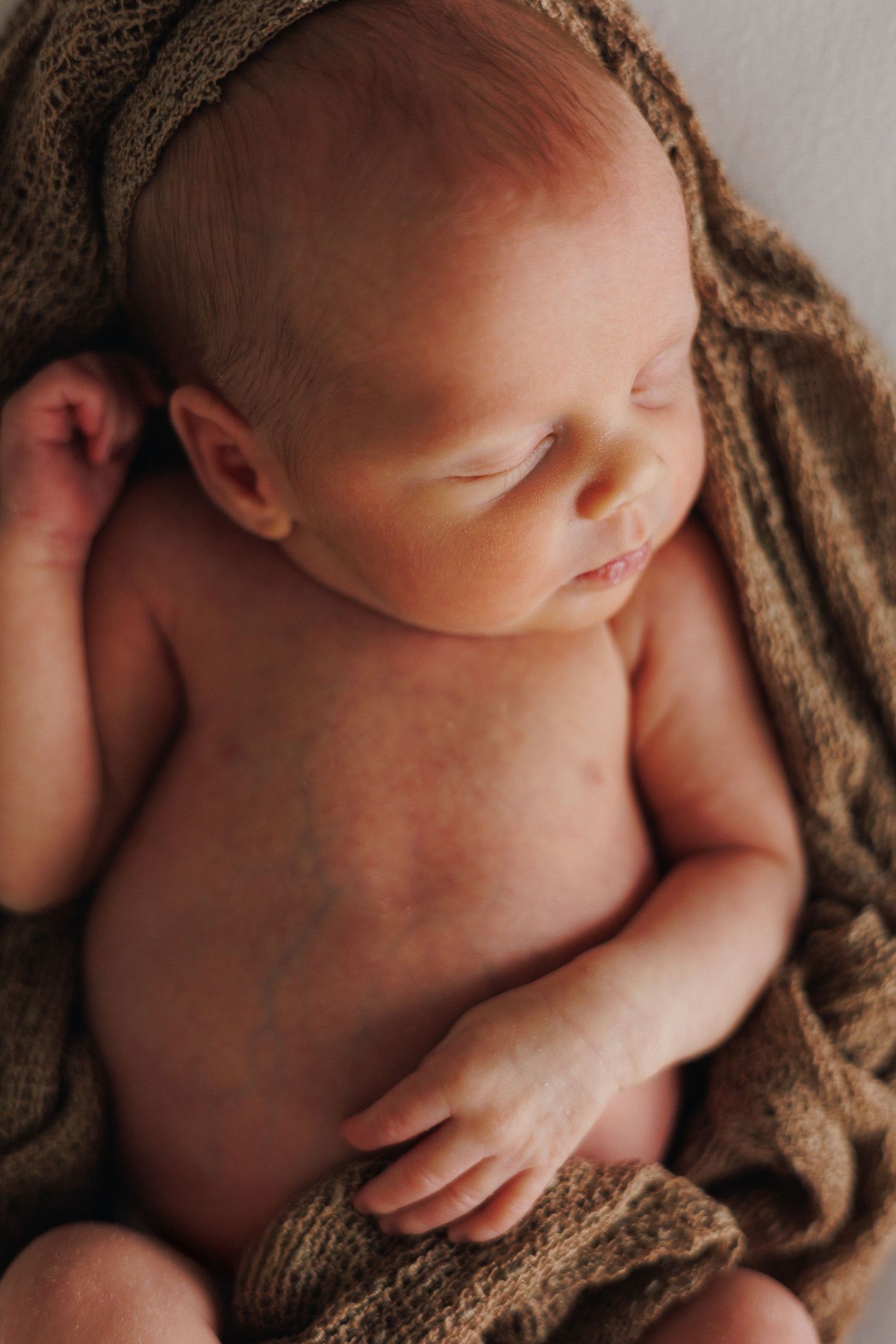 Peaceful sleeping newborn baby wrapped in a soft brown knit blanket, captured in a serene newborn photography portrait.