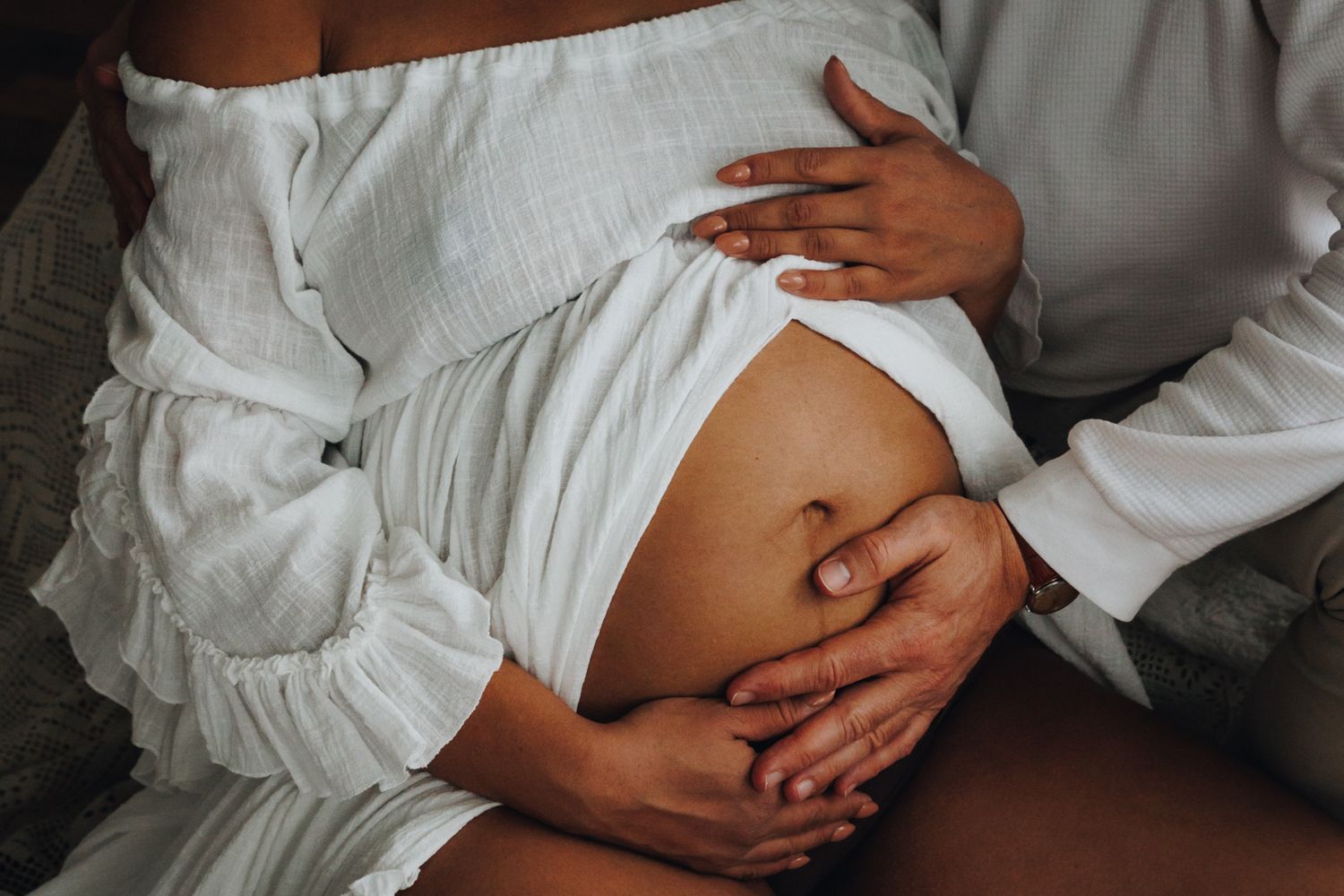 Close-up series of hands gently caressing a pregnant belly through white fabric in natural light.