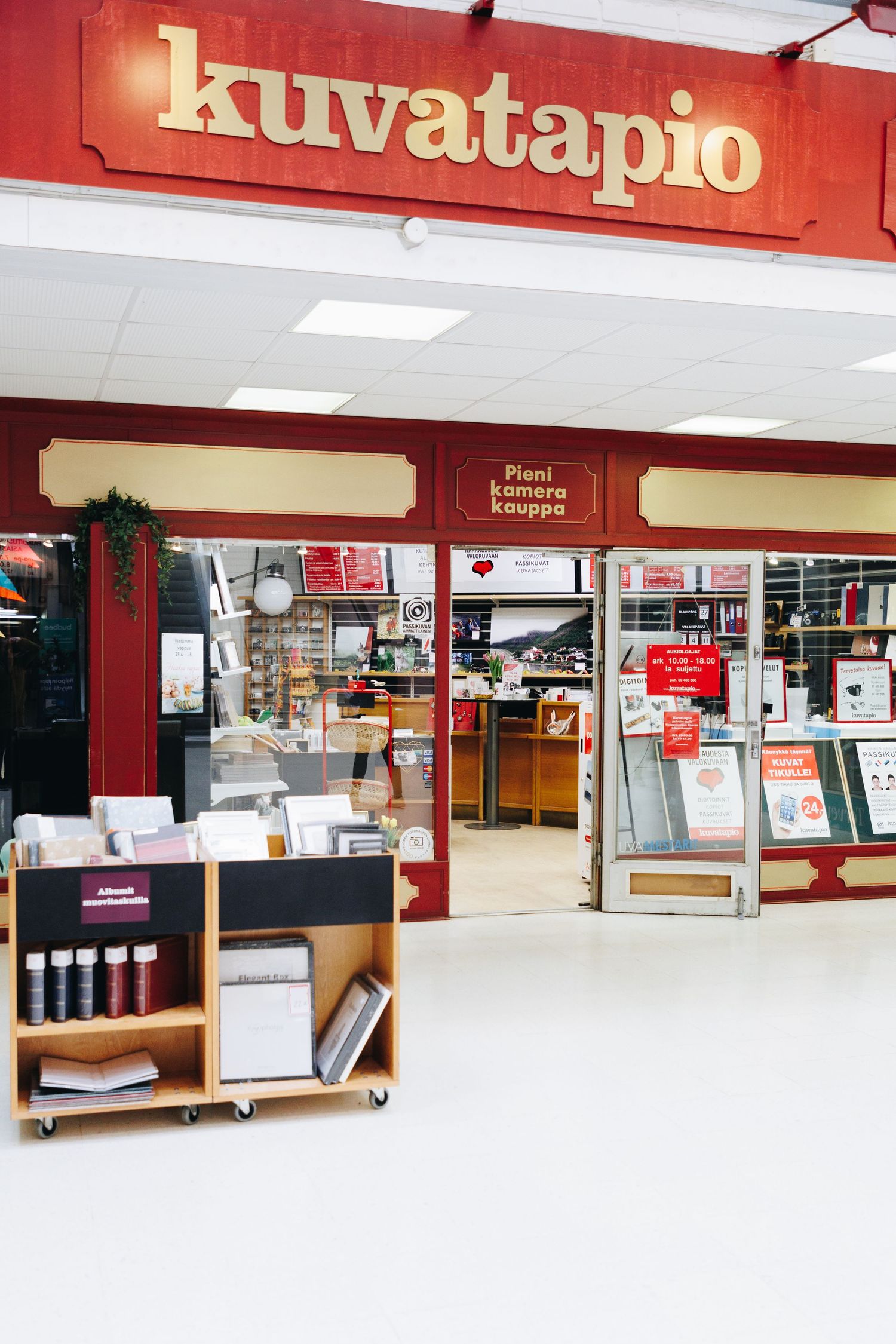 Kuvatapio camera shop entrance in a Finnish mall with red signage, display shelves, and holiday decorations.