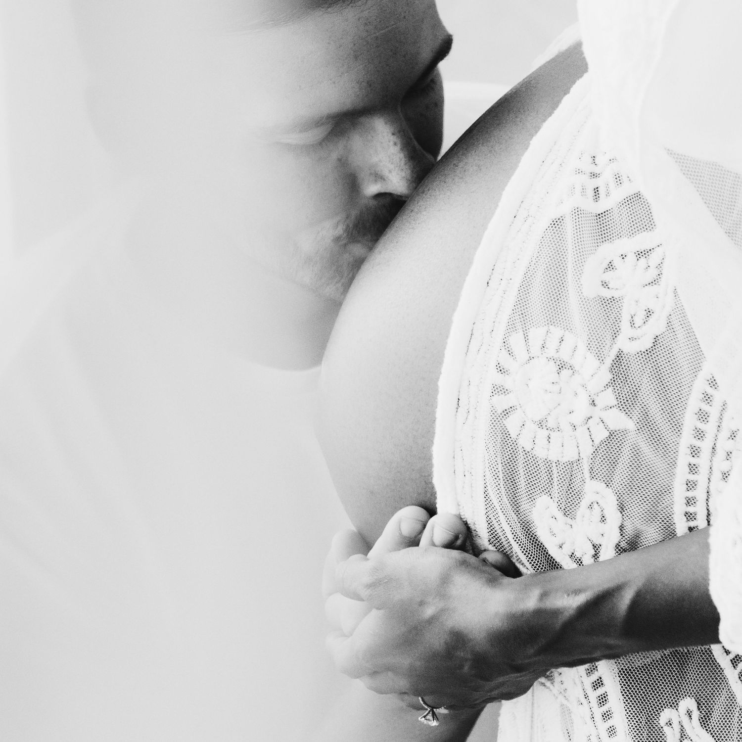 Intimate black and white maternity photo showing a tender kiss on a pregnant belly with delicate lace details.