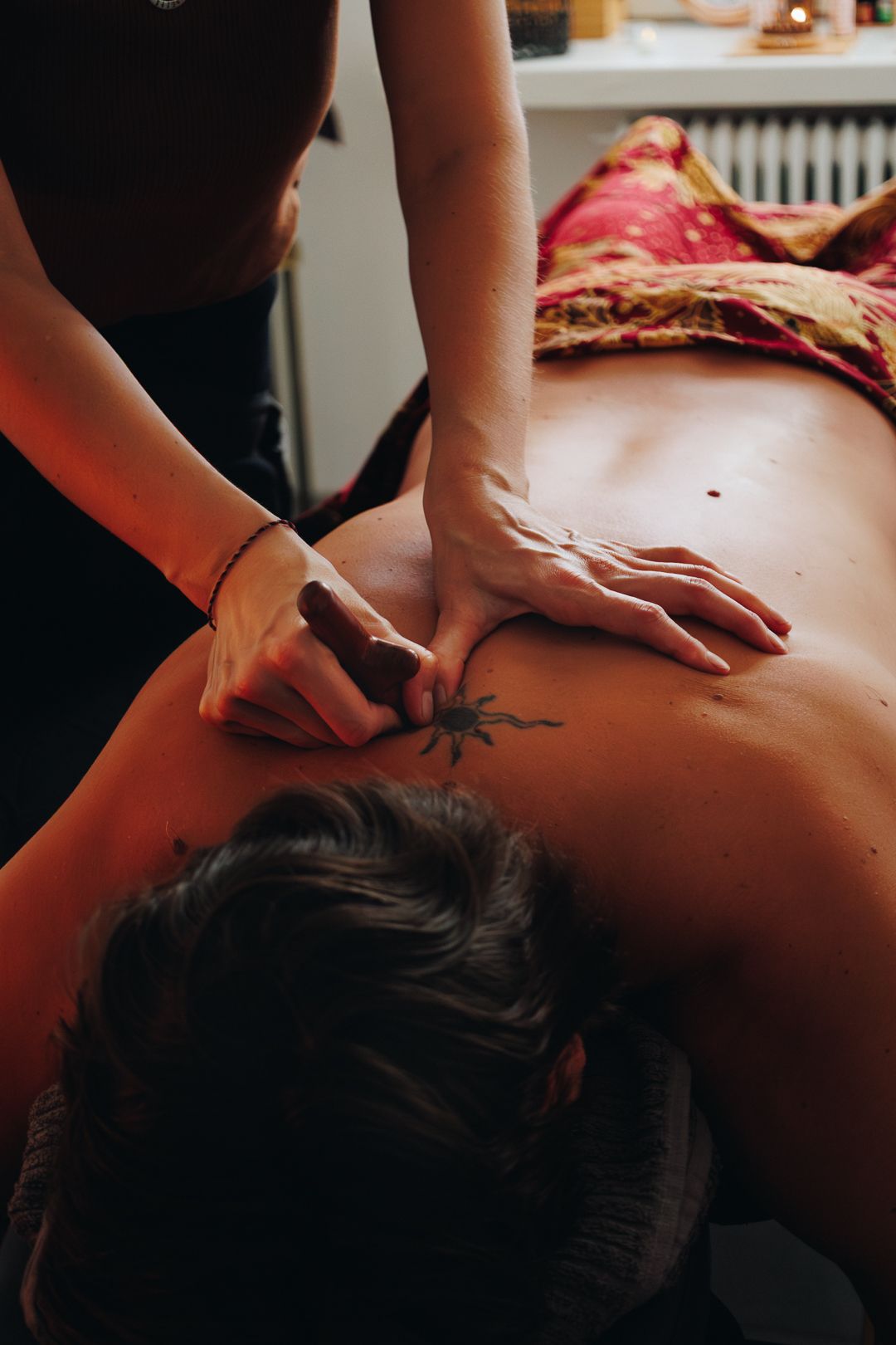 Massage therapist applying deep tissue techniques to the upper back of a client with a tattoo.