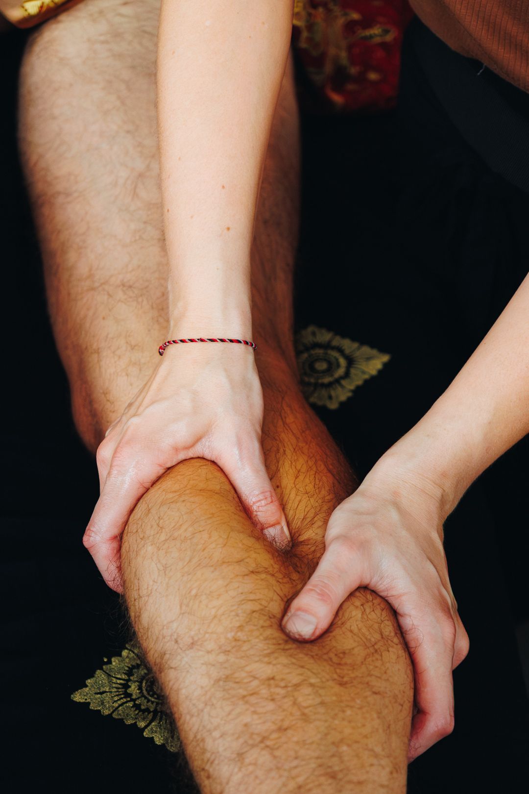 Close-up of a massage therapist using both hands to massage a client's knee and lower leg.