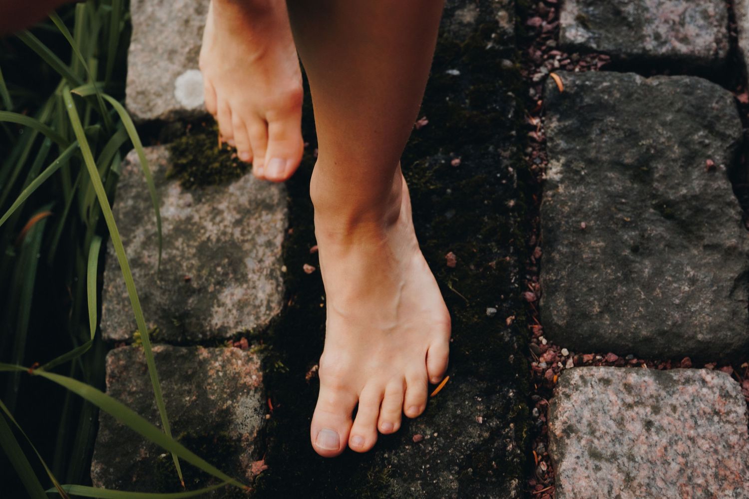 Bare feet standing on mossy stone pavers surrounded by lush green plants in a garden setting.