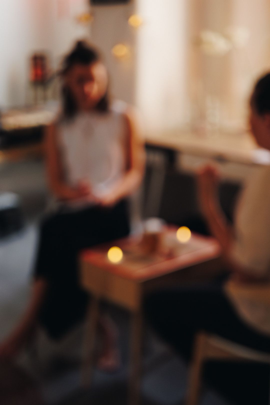 Two people sitting at a small candlelit table in a cozy cafe, enjoying an intimate conversation.