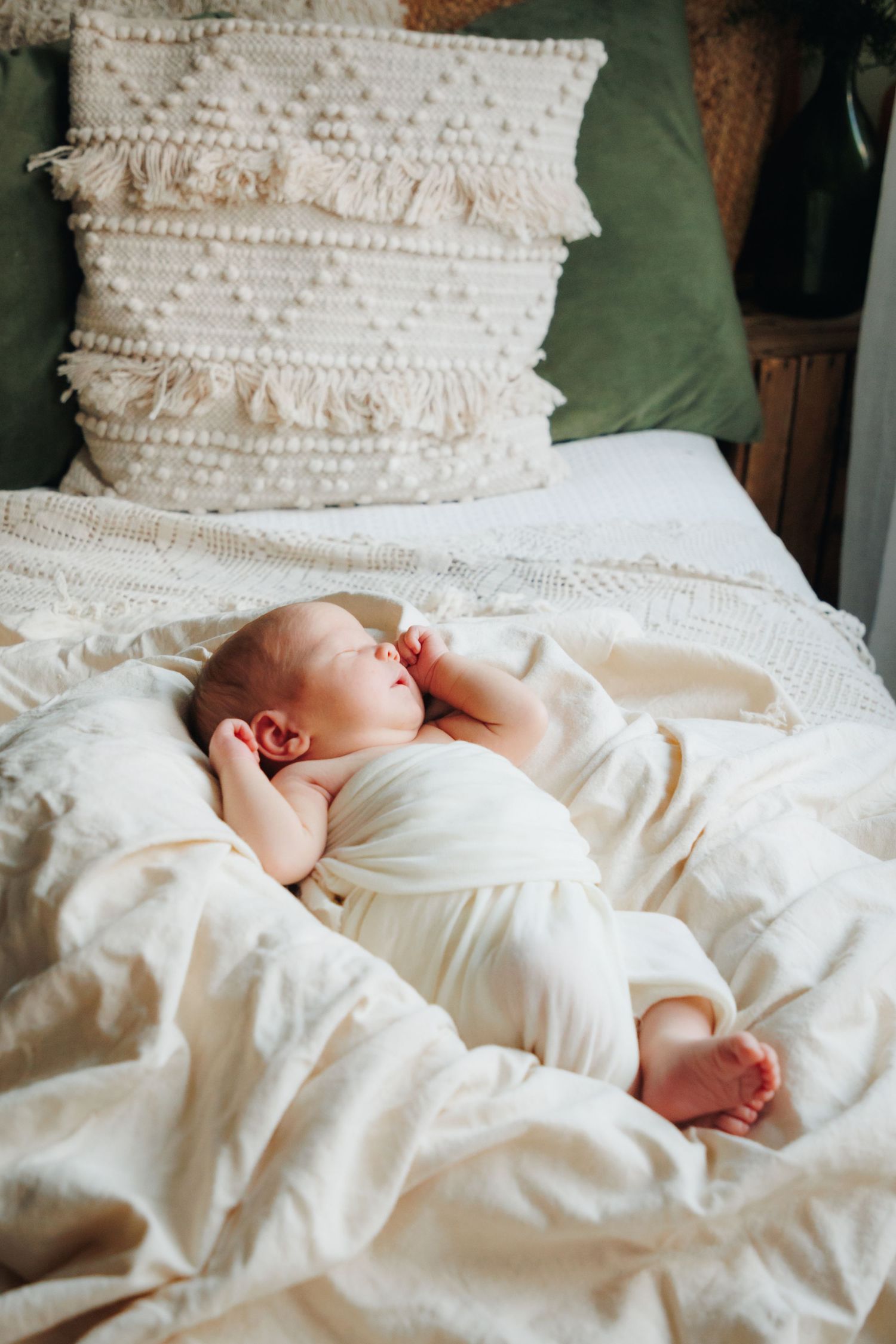 A baby sleeping peacefully on white textured pillows with ruffled details.