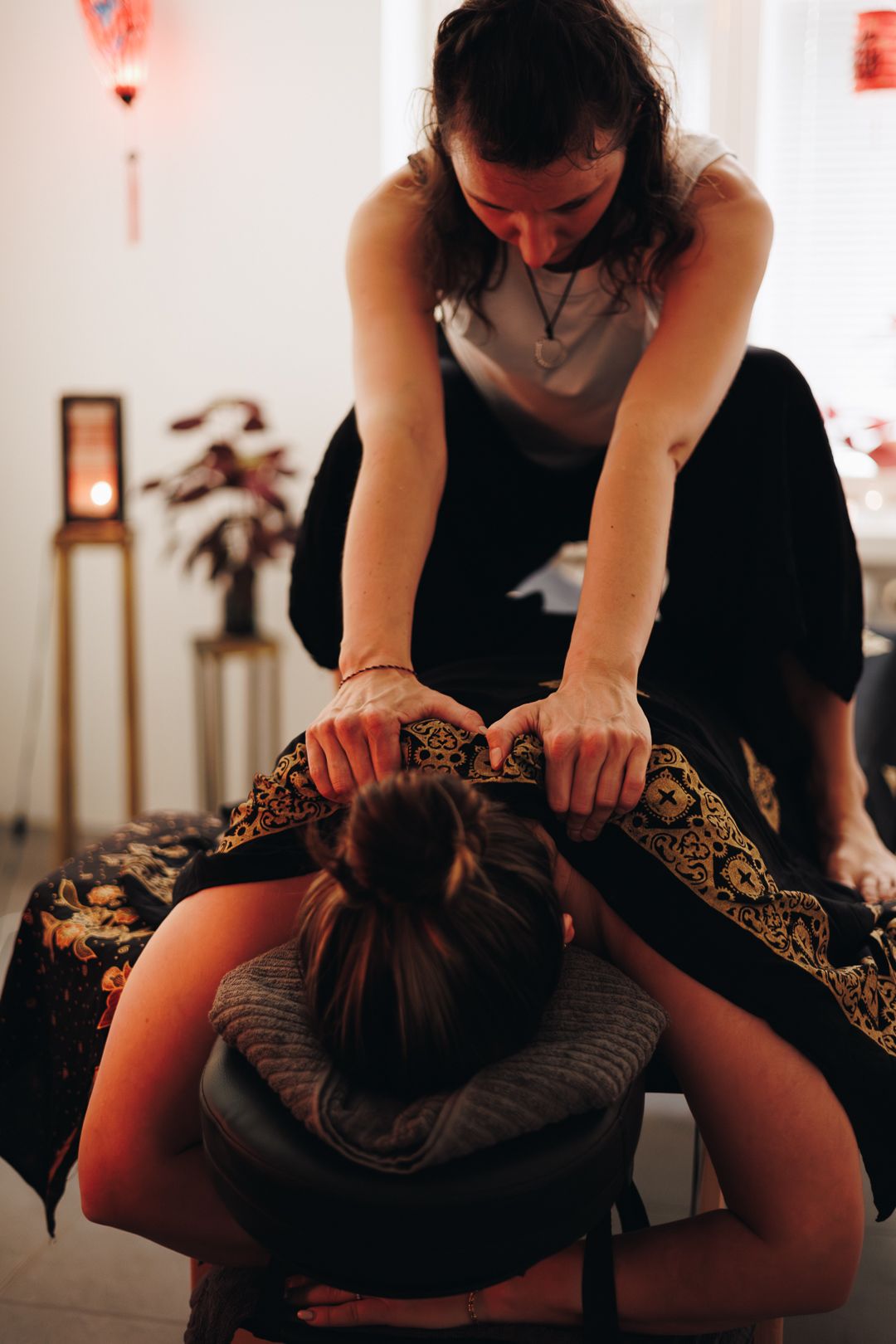 A massage therapist performs a back massage on a client seated in a massage chair during a spa treatment session.