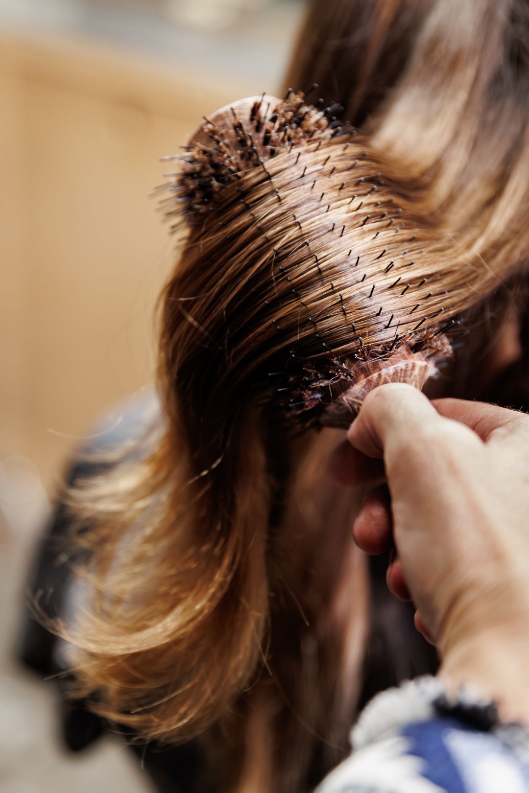 Close-up of hairstylist brushing long brown hair with round bristle brush in salon.