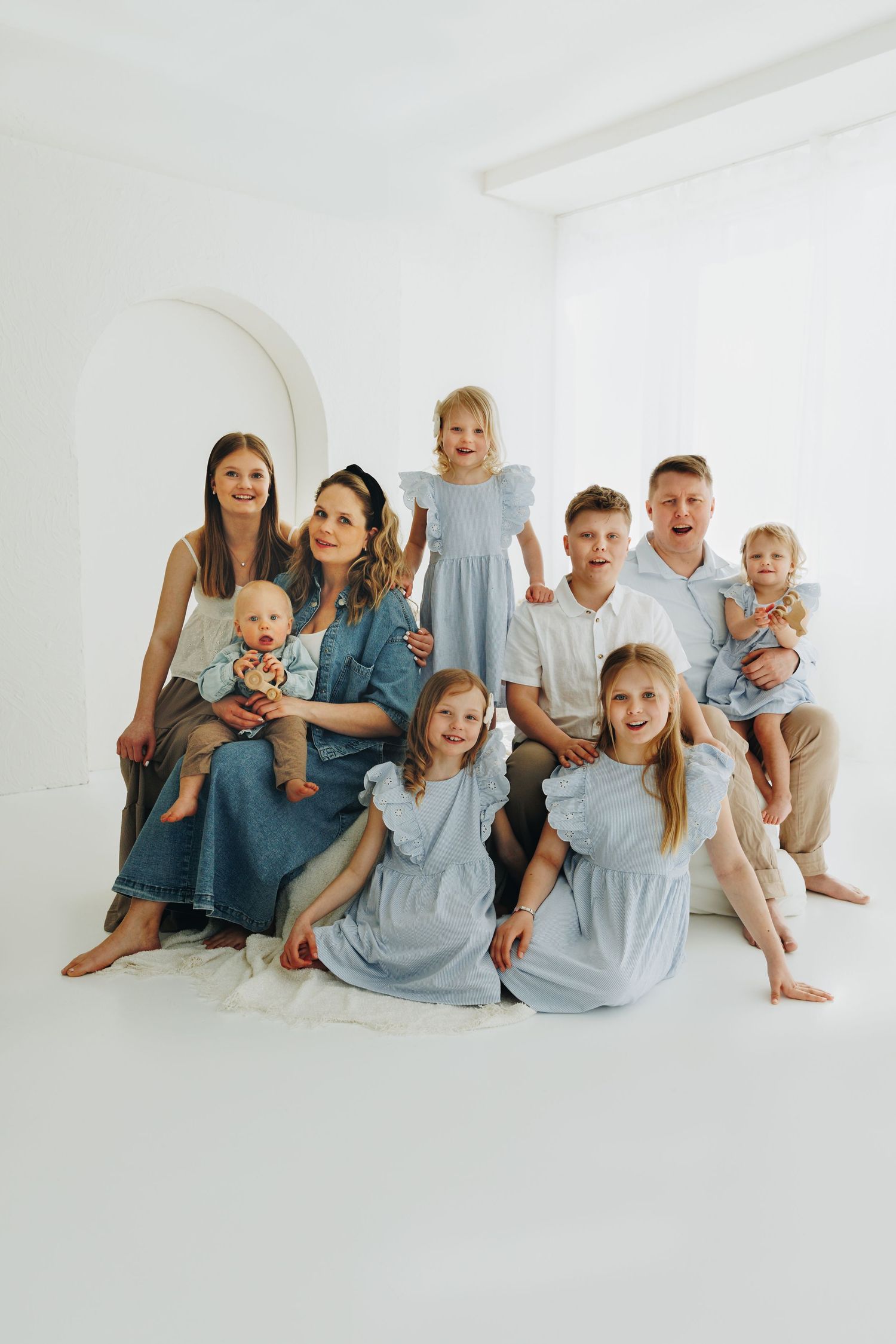 Large family with children posing together in a bright white studio, wearing coordinated blue and white outfits.