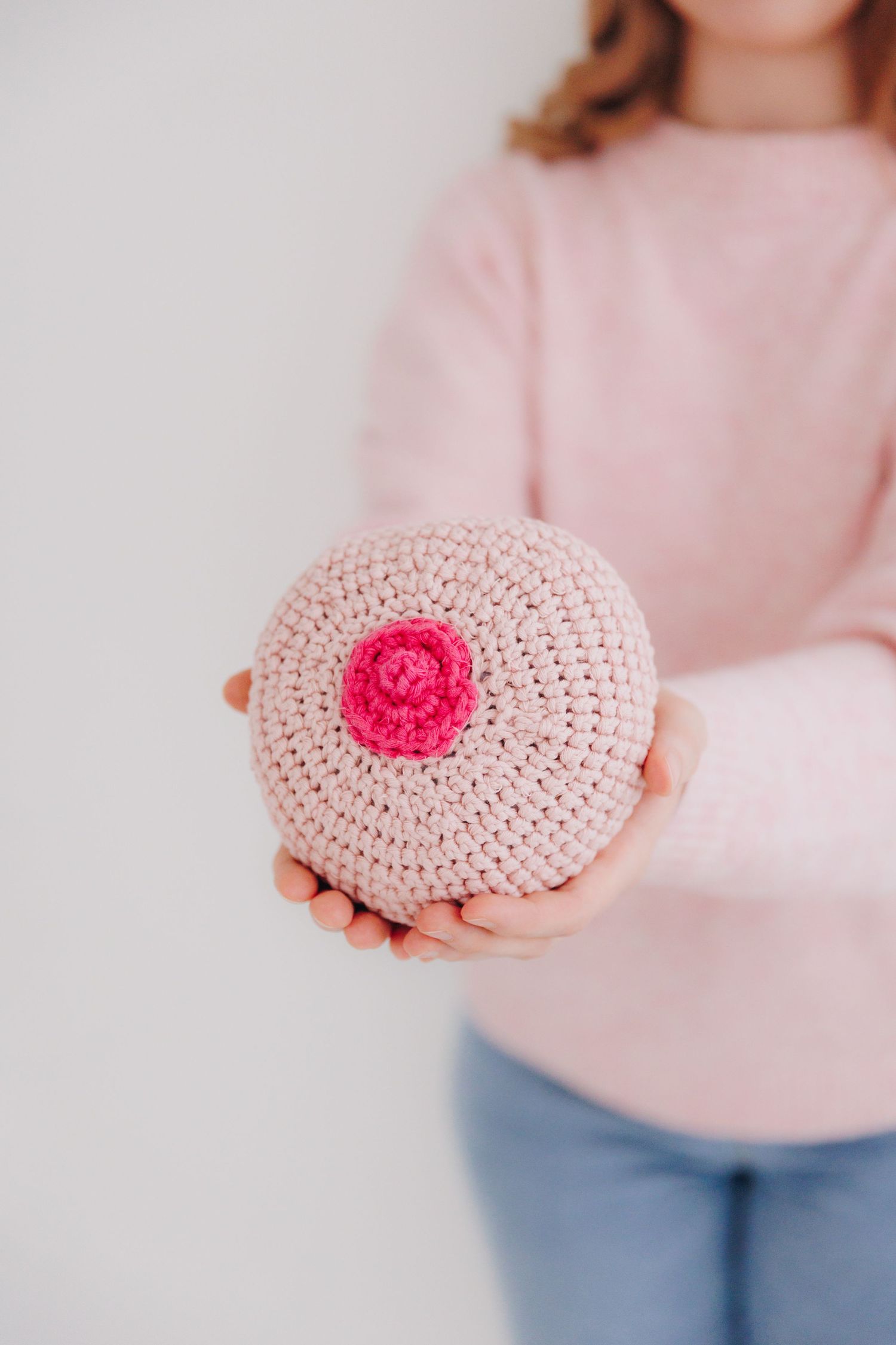 Person holding a crocheted breast model in pink yarn, used for breastfeeding education and awareness.