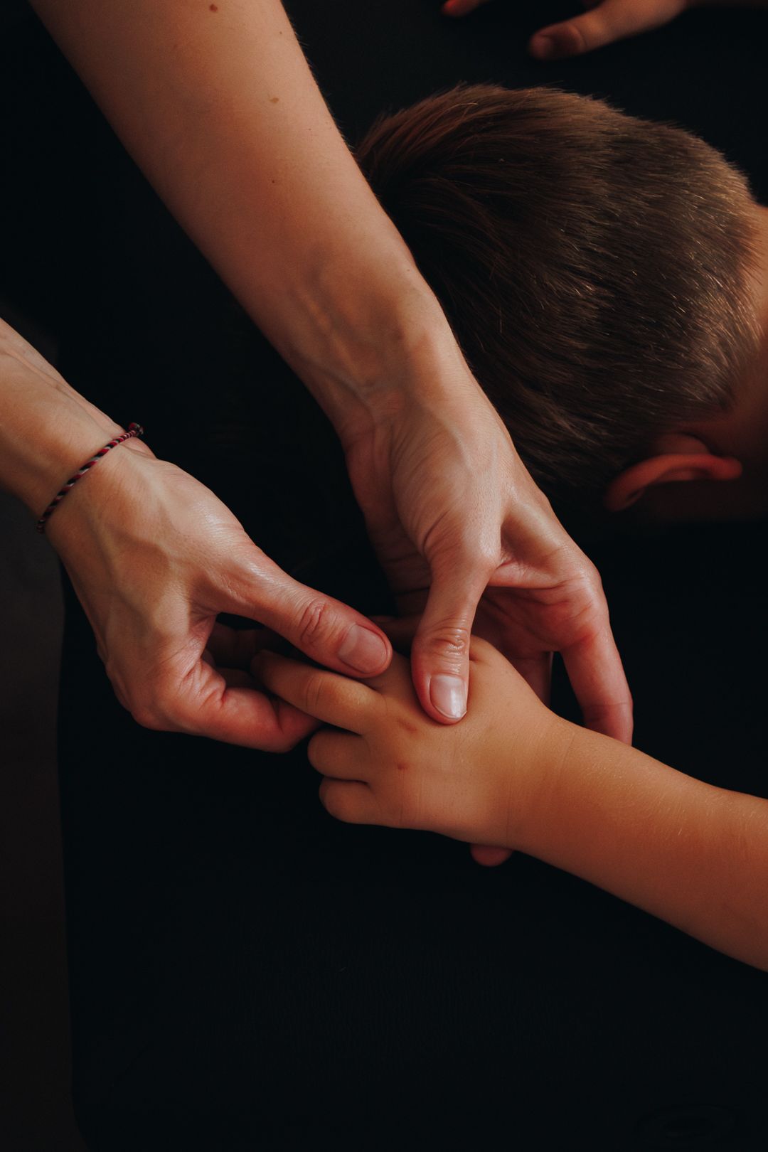 Therapist applying acupressure finger massage technique on child's hand in dark studio setting.