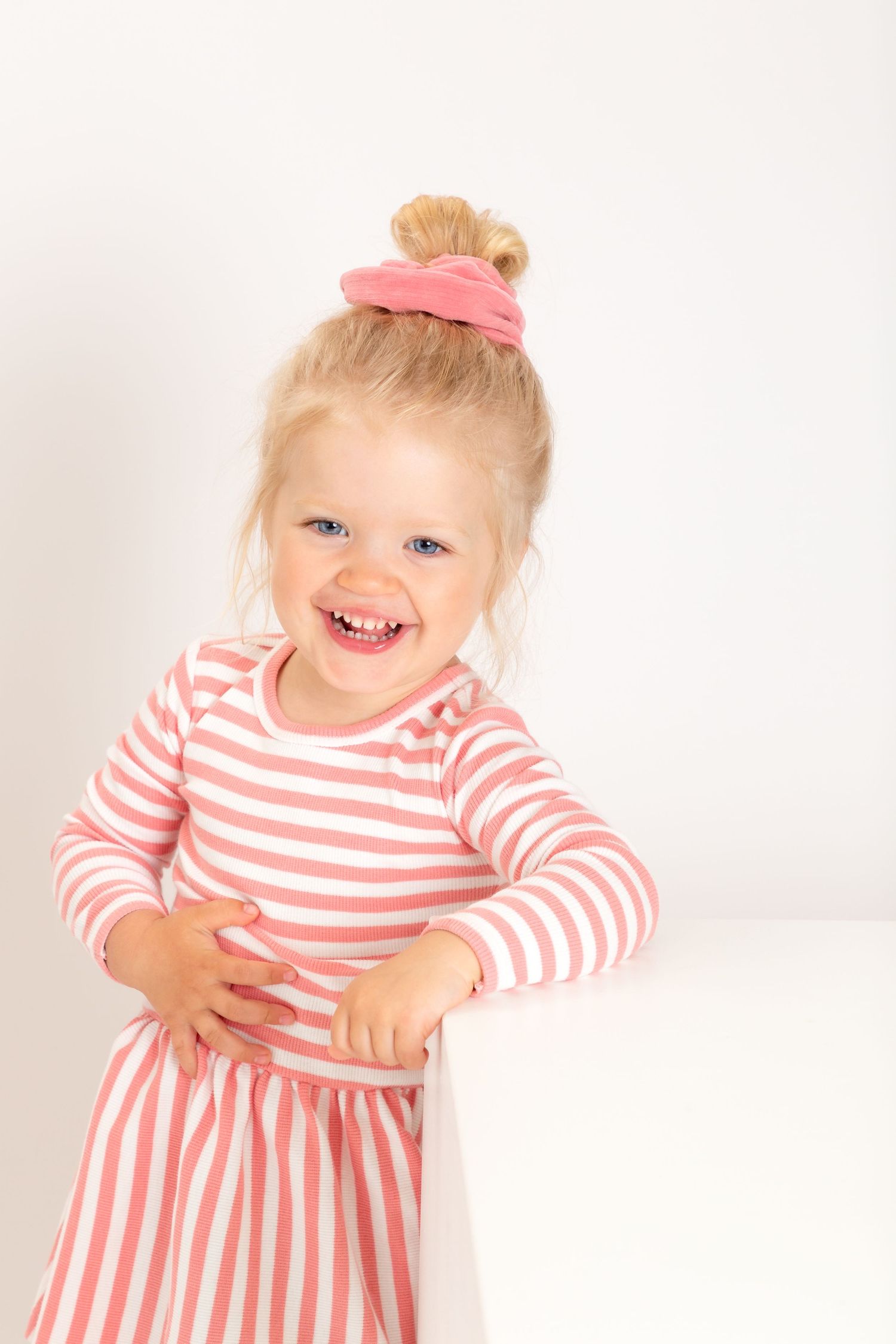 A small child wearing a pink and white striped dress smiles and poses against a white backdrop in a series of photos.