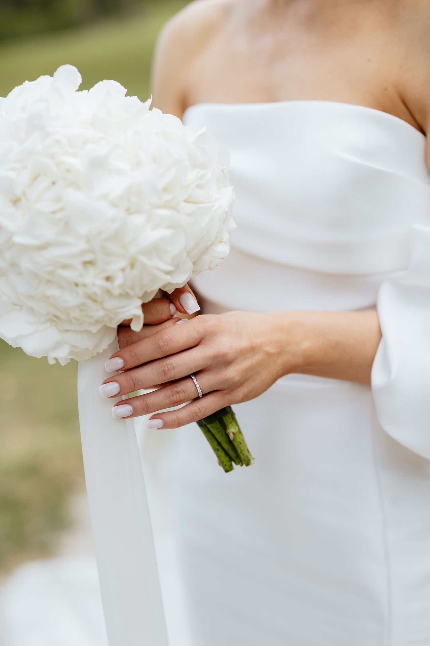 Close-up of bride's hands holding a white hydrangea bouquet with wedding ring detail.