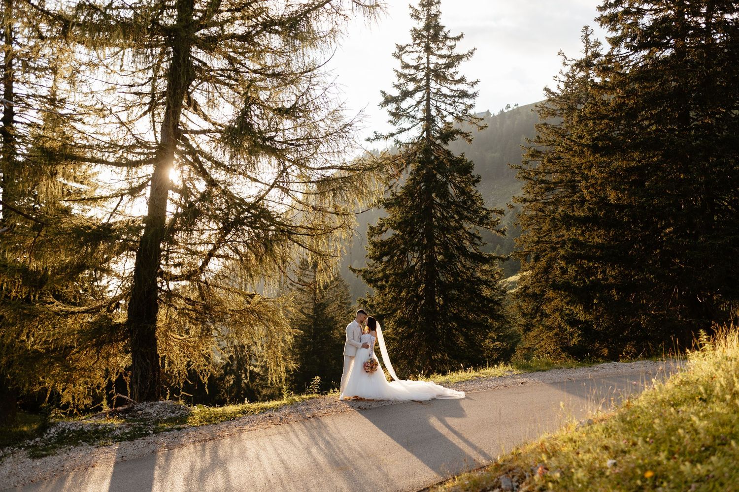 A scenic mountain wedding photo showing a figure in white on a winding forest path.