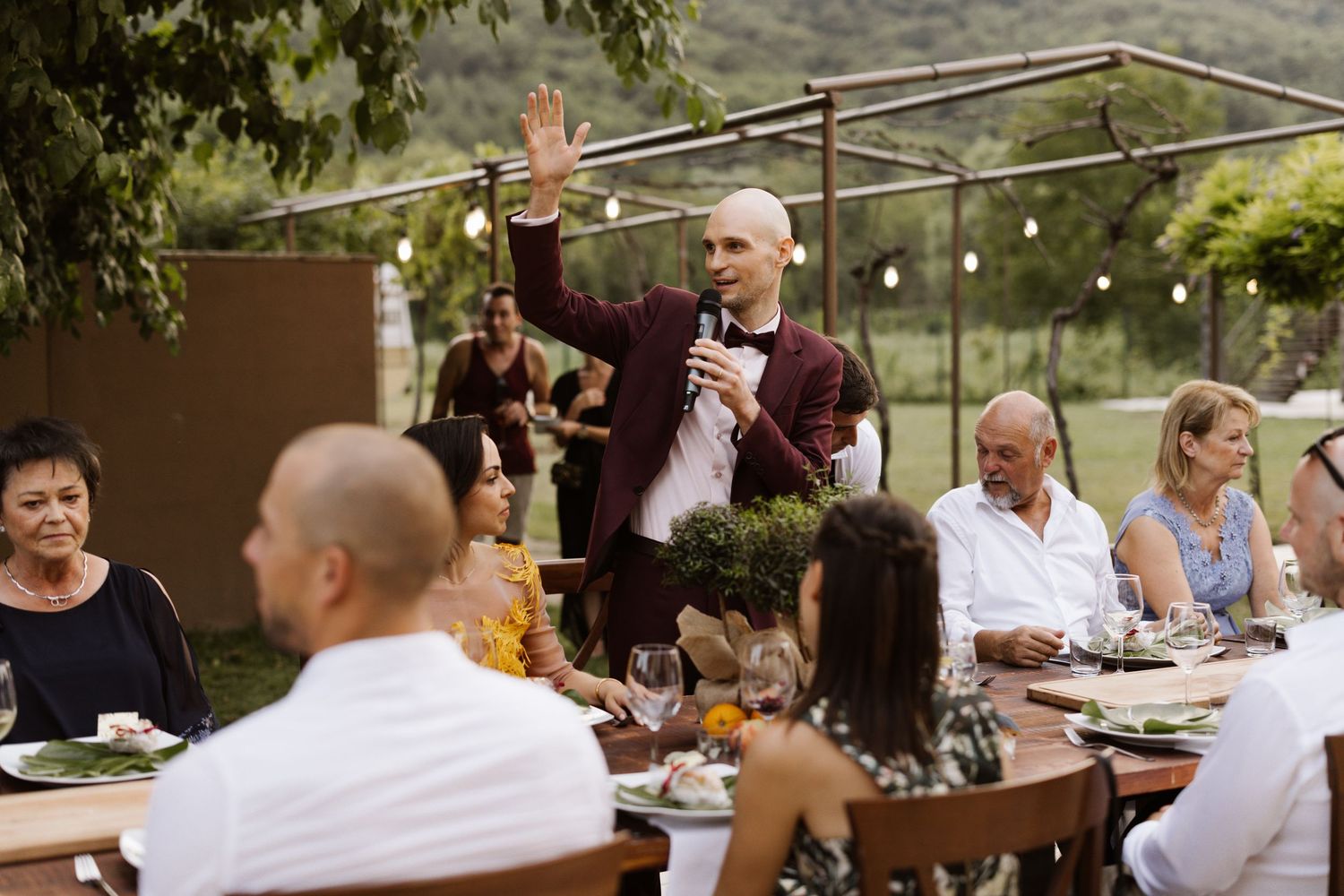 Outdoor dinner party setting with guests seated at long tables under string lights.
