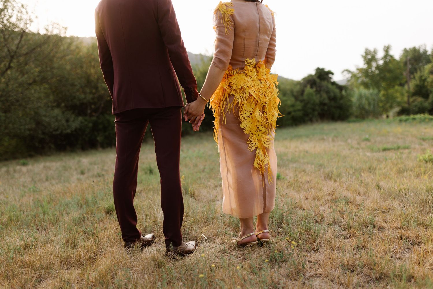 Wedding party members standing in field wearing burgundy and yellow attire.
