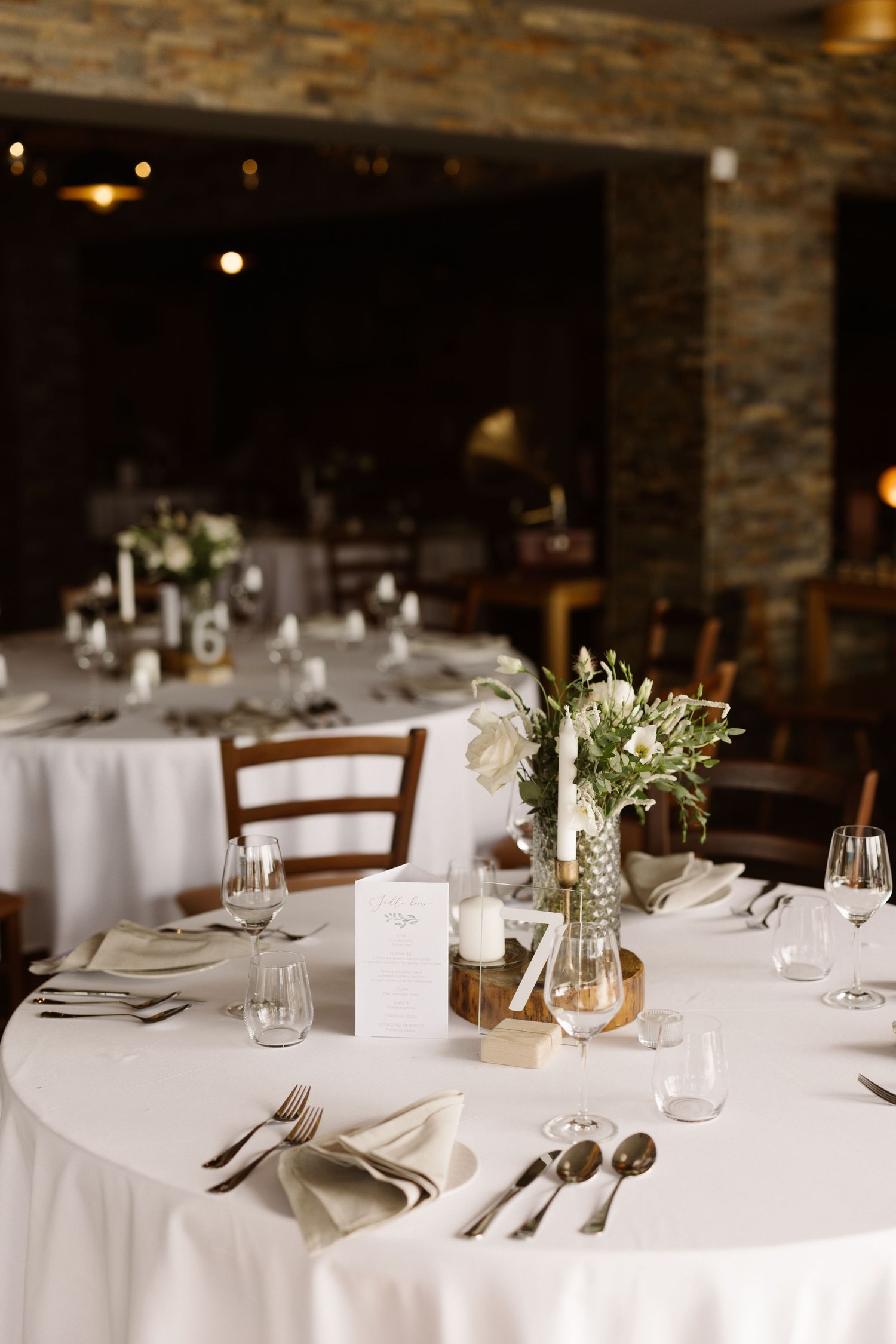 Elegant wedding reception tables set with white linens, glassware and delicate floral centerpieces in a rustic stone venue.