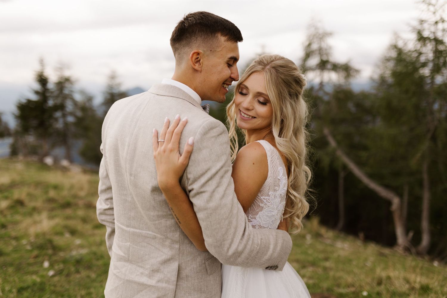 A romantic couple embraces in an outdoor setting with natural lighting and scenic landscape views.