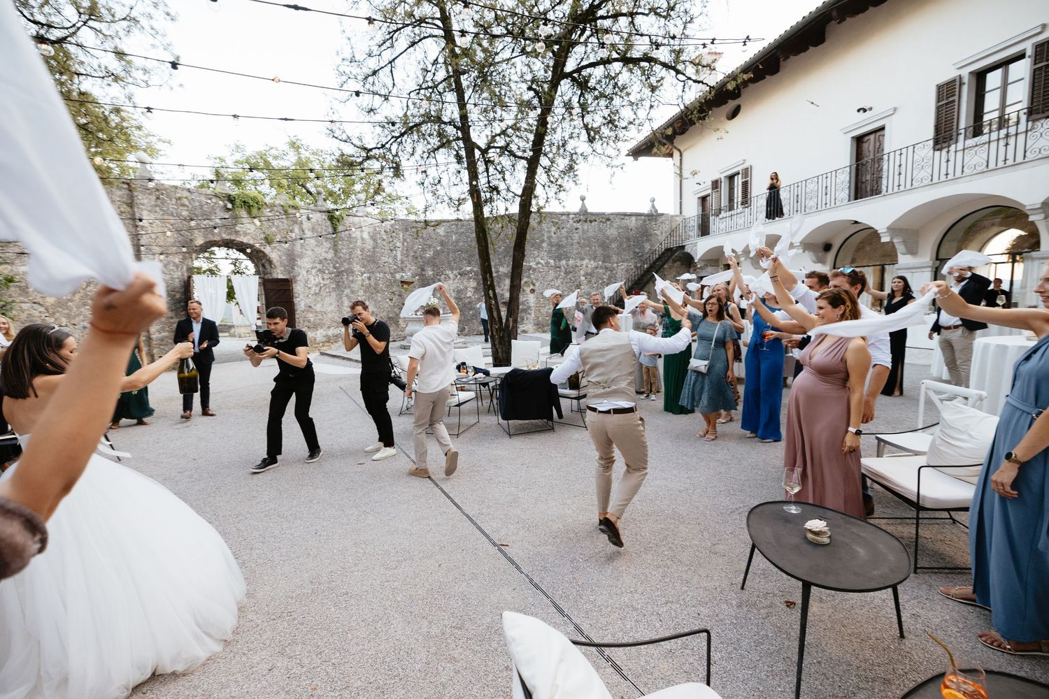 Wedding guests dance and celebrate at an outdoor reception under string lights and trees.