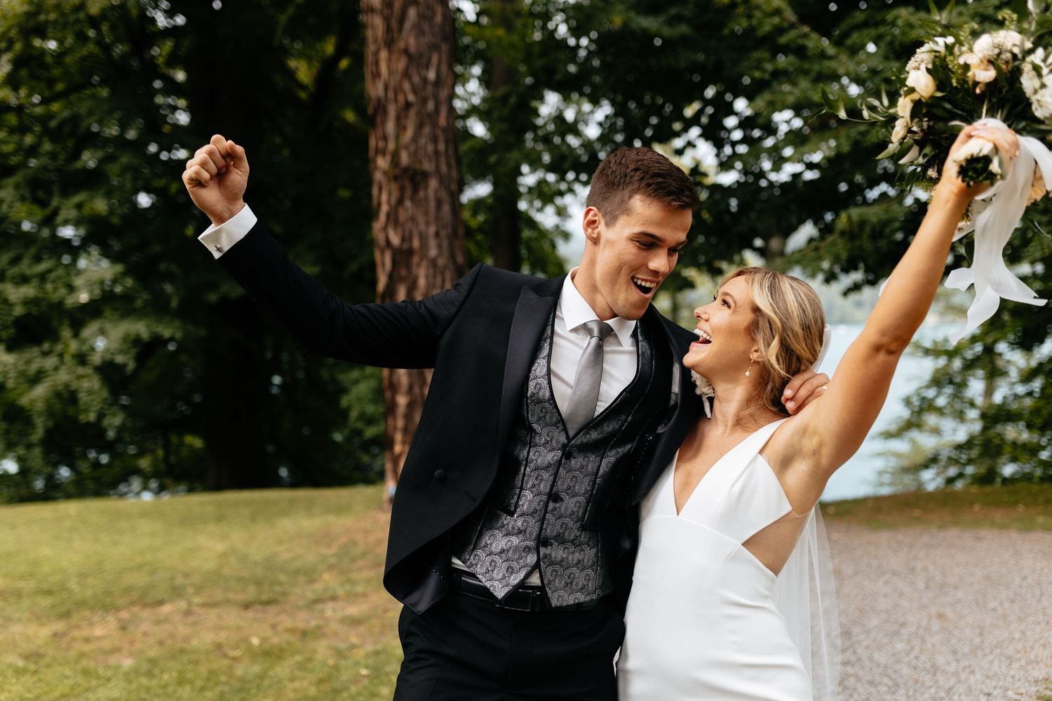 Joyful newlyweds celebrating with raised arms in an outdoor garden setting.