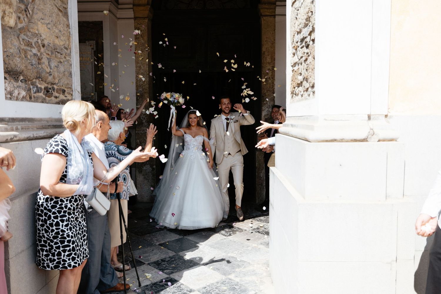 Wedding guests gather outside stone building entrance for celebration.