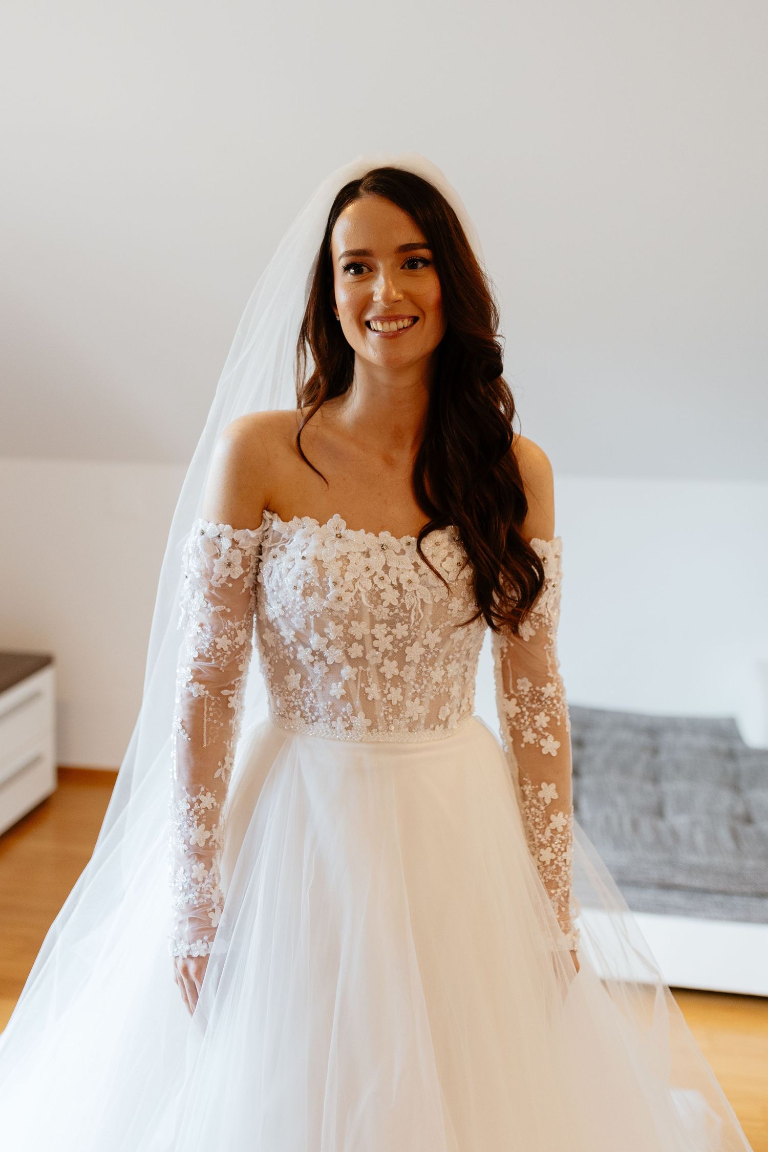 A stunning off-shoulder wedding dress with delicate floral lace sleeves and a flowing tulle skirt.