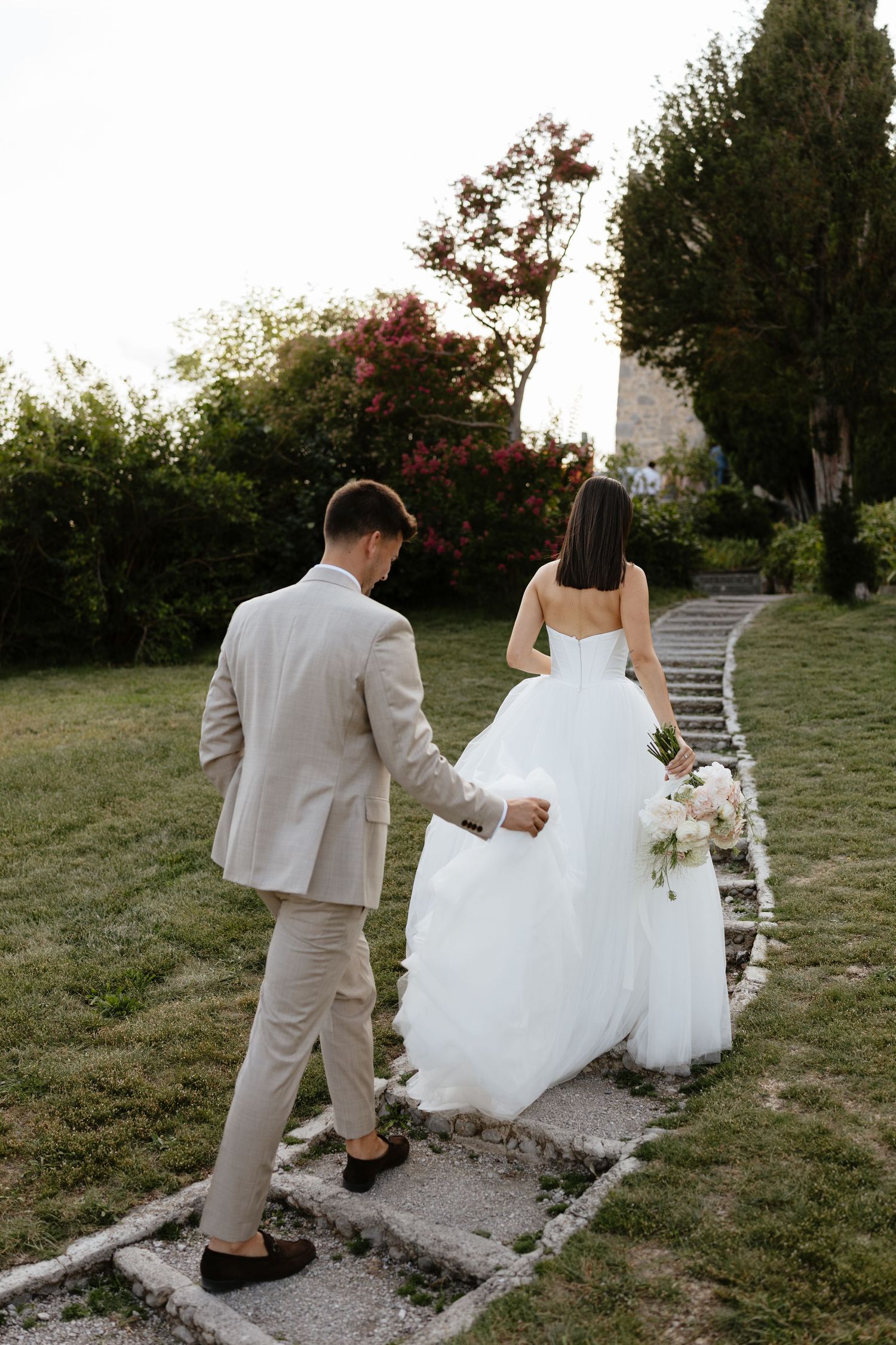 Couple walks down stone path surrounded by lush garden greenery.