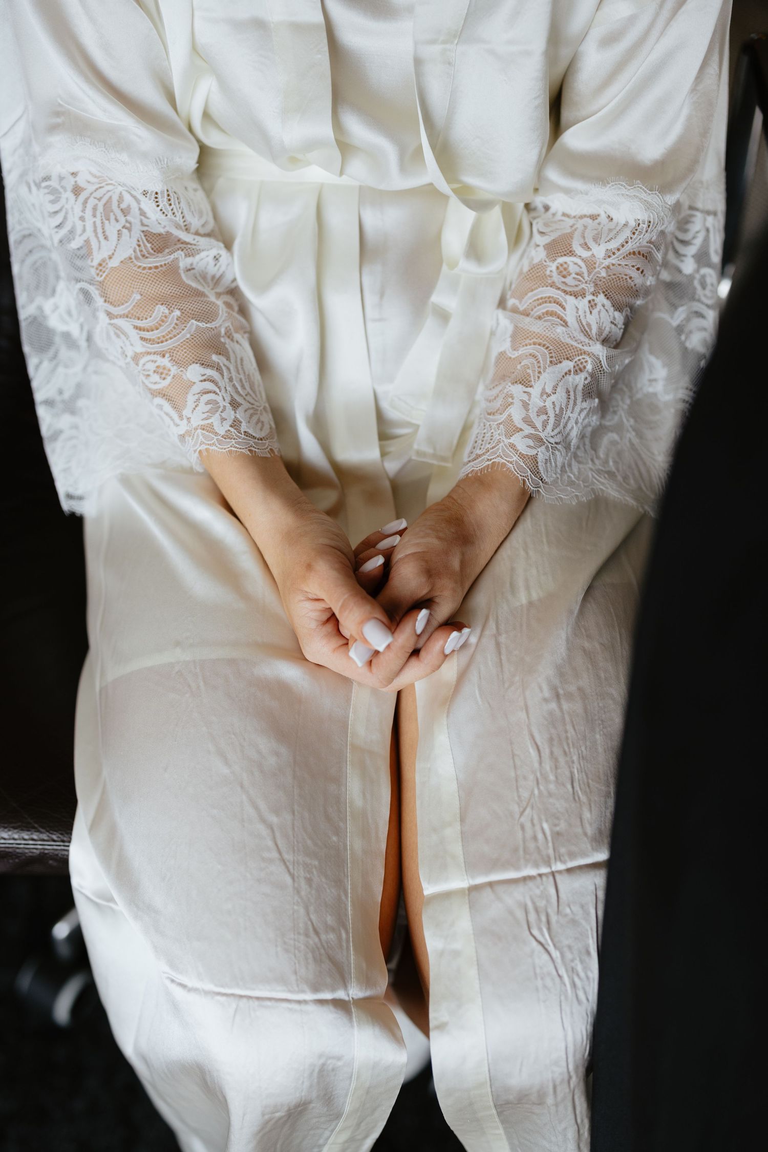Close-up of delicate lace details on a white wedding dress with clasped hands.
