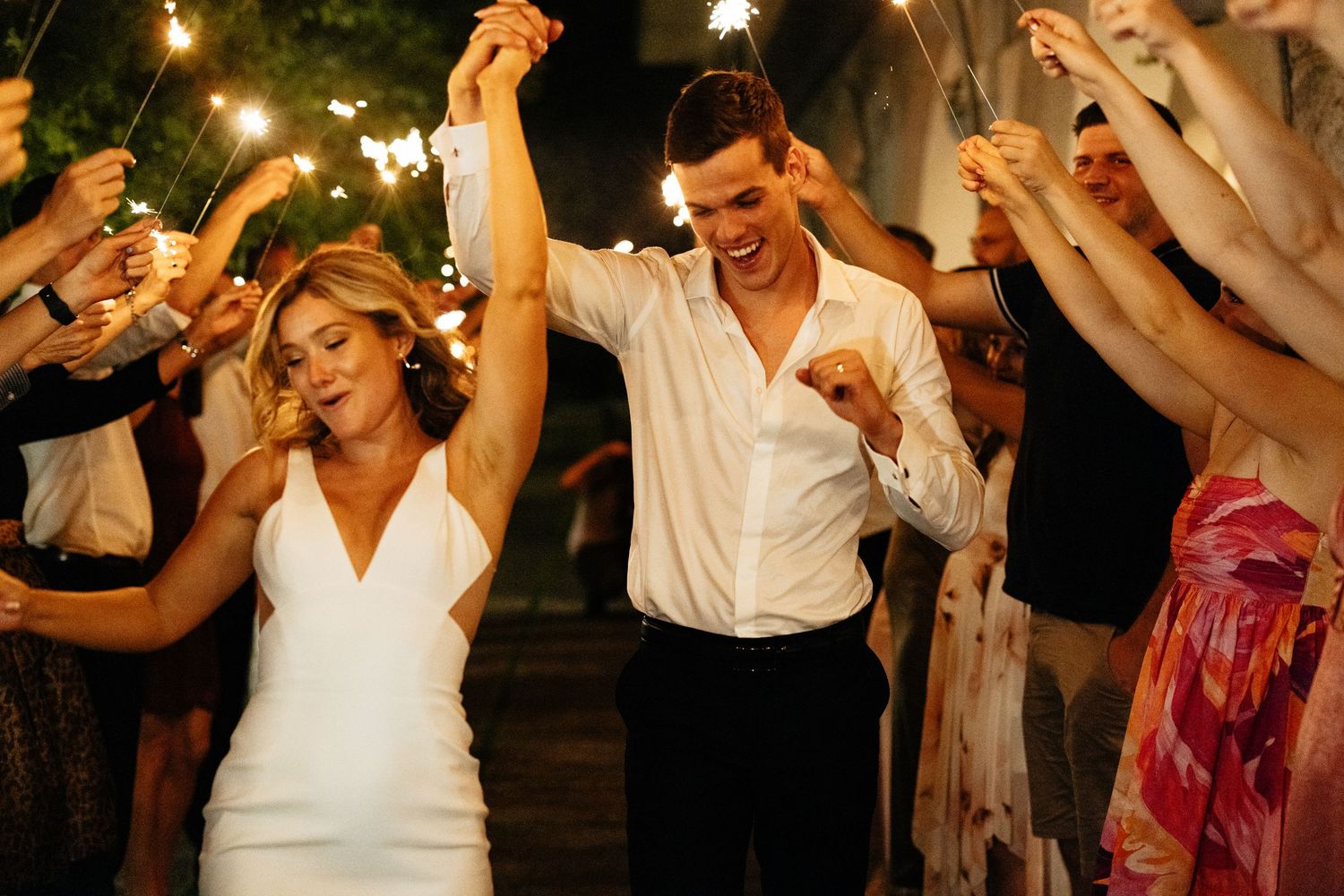 Wedding couple dancing with sparklers at night surrounded by celebrating guests.