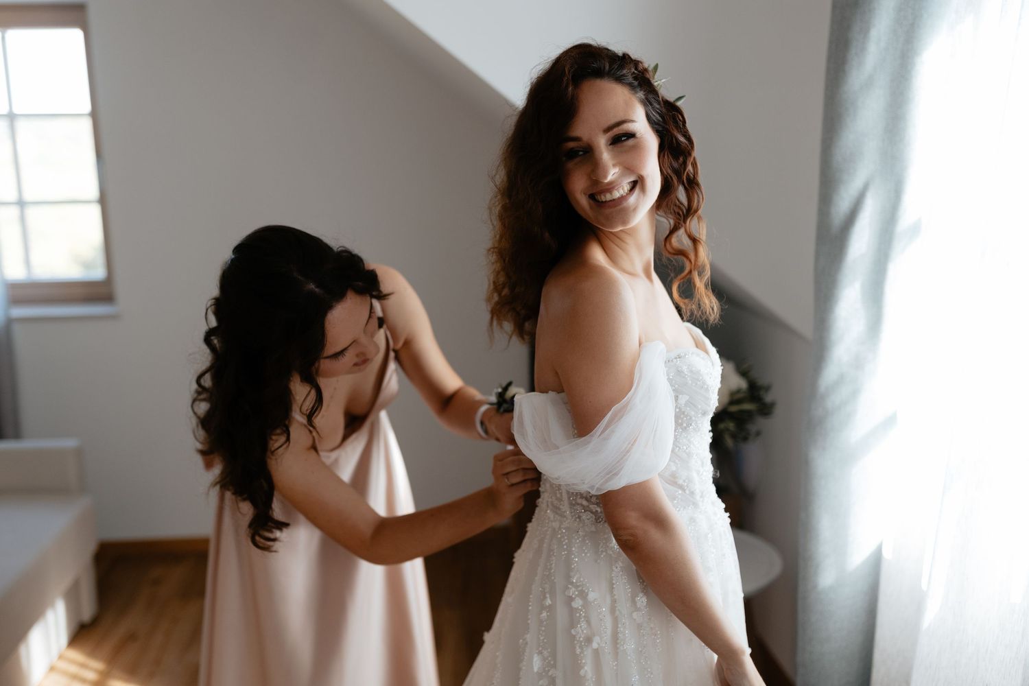 Two people in white dresses share a joyful moment while dancing together in a bright sunlit room.