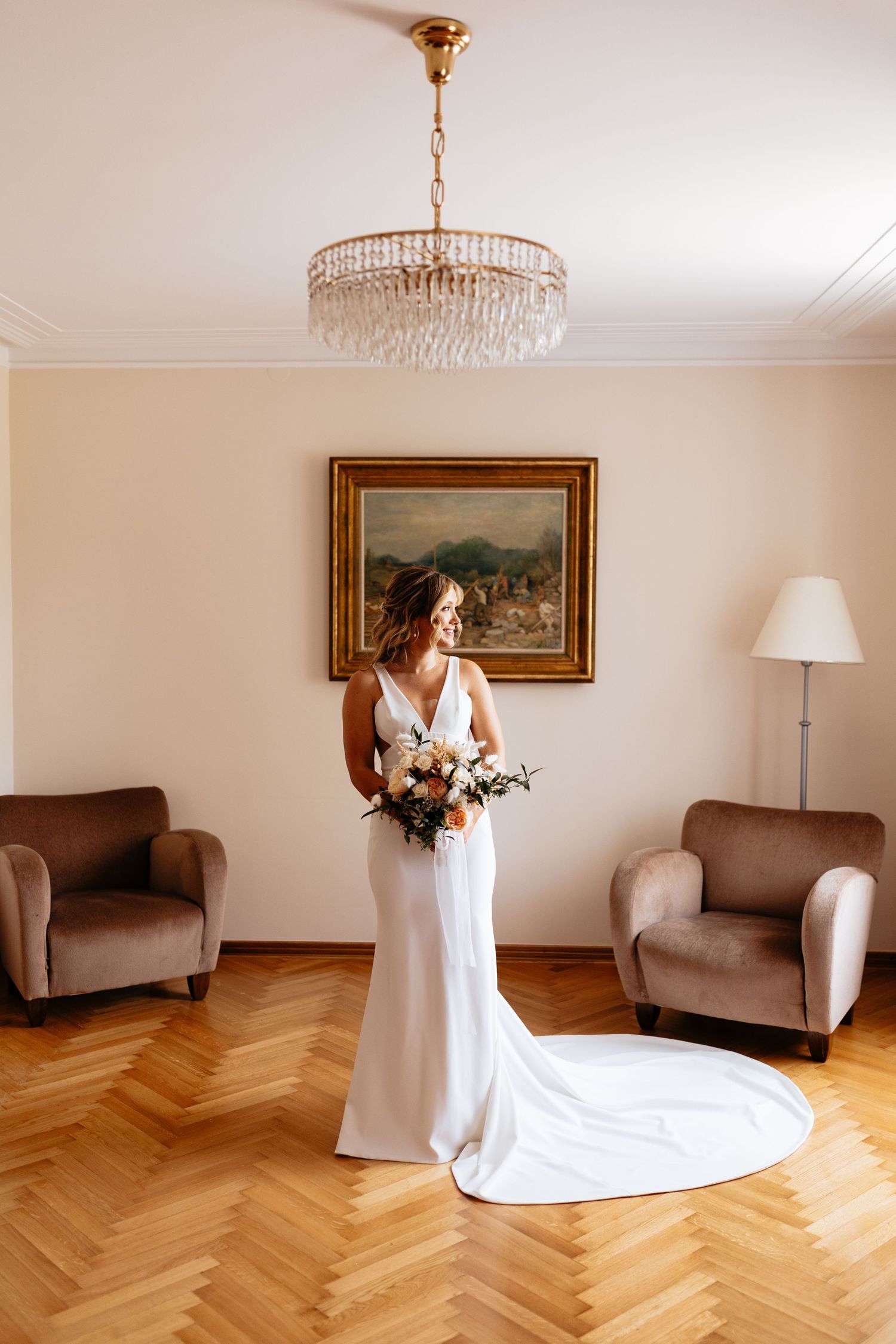 Elegant bridal portrait in a room with herringbone floors, crystal chandelier and brown armchairs.