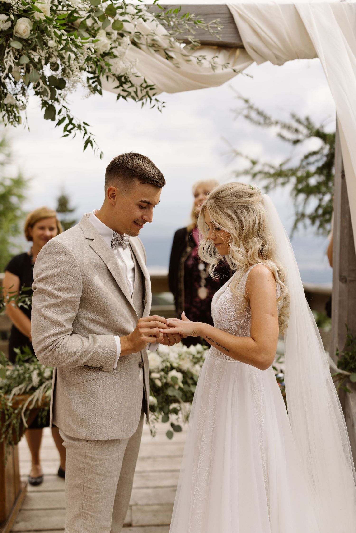 Couple in light gray suit and white dress sharing an intimate moment under a draped outdoor canopy.