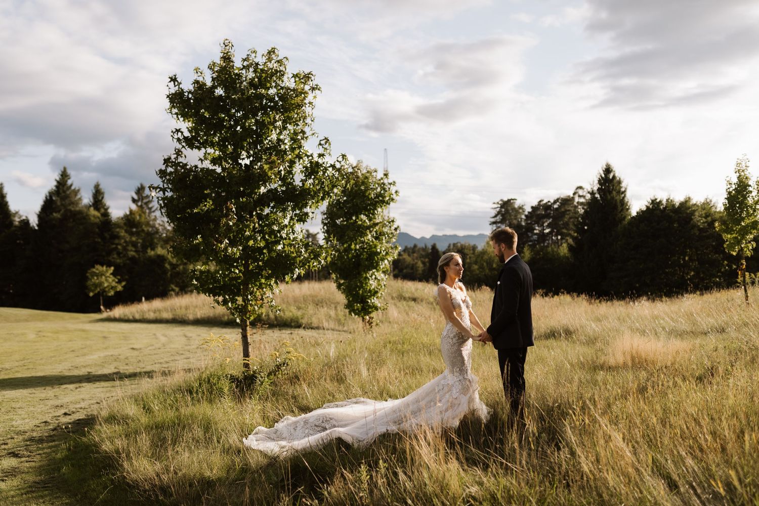 Wedding couple walking through a scenic field with mountains and dramatic clouds in the background.