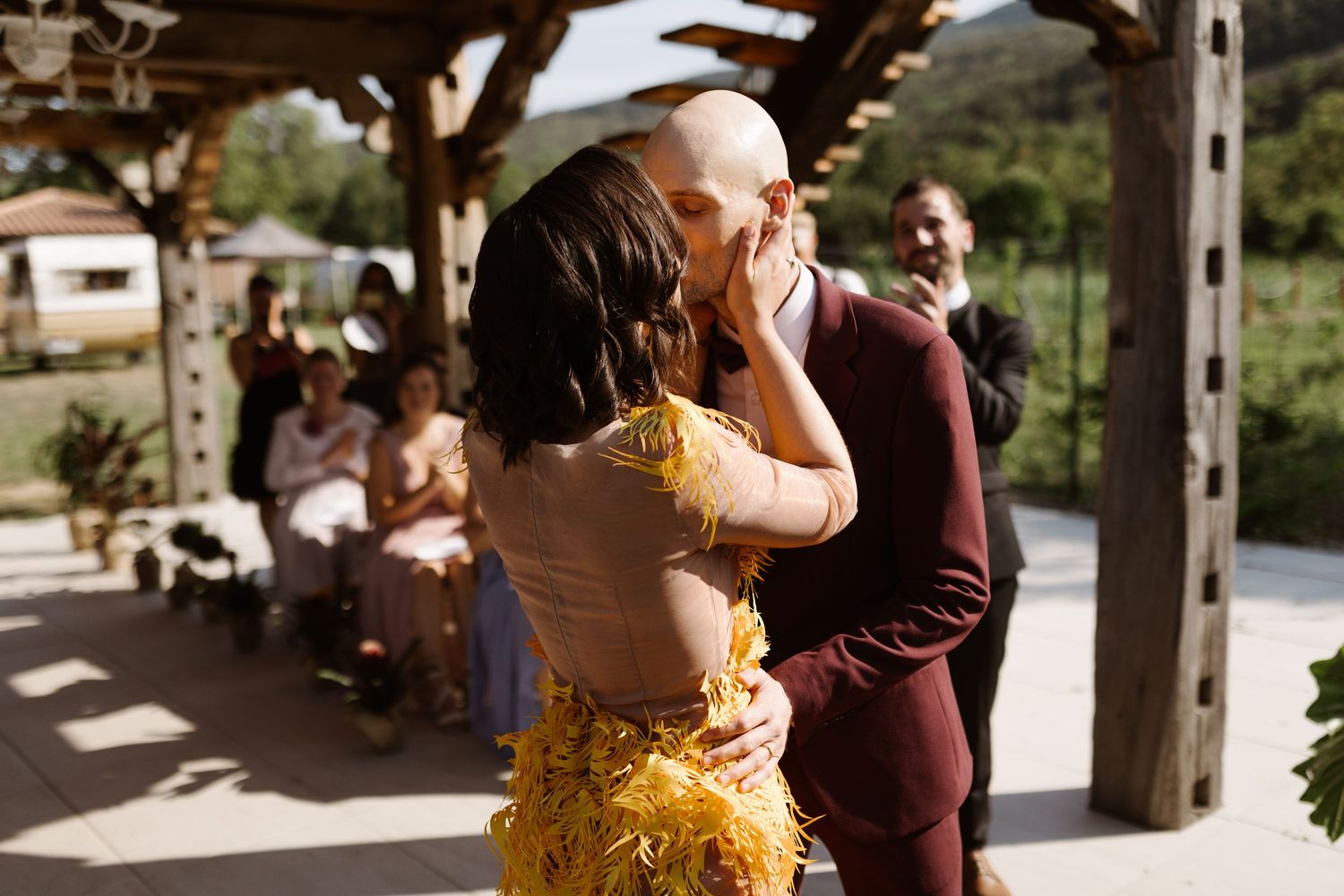 Couple in burgundy and yellow outfits dancing together on a sunlit outdoor patio.