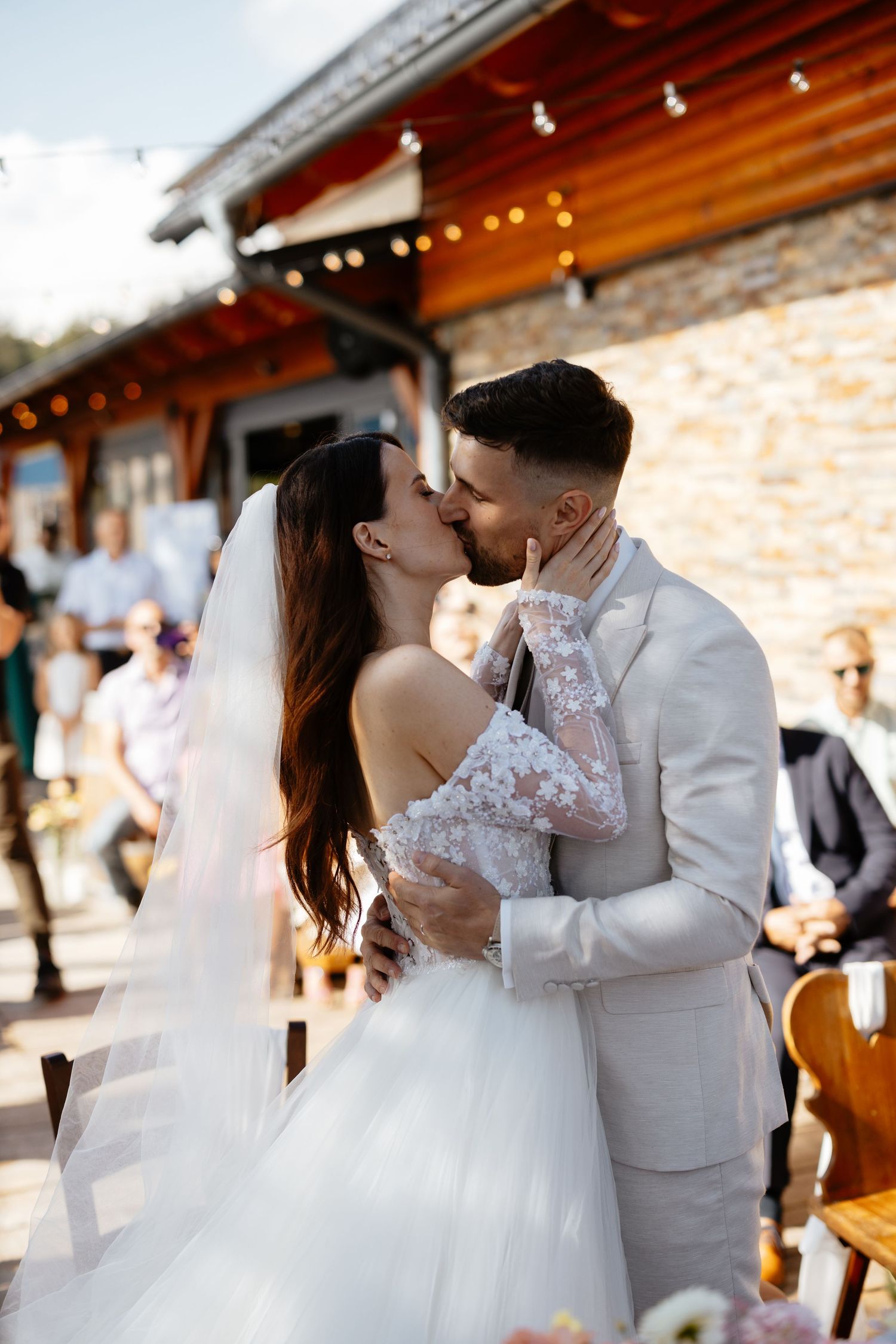 A romantic wedding couple shares intimate kisses in a rustic venue with warm wooden beams and string lights.